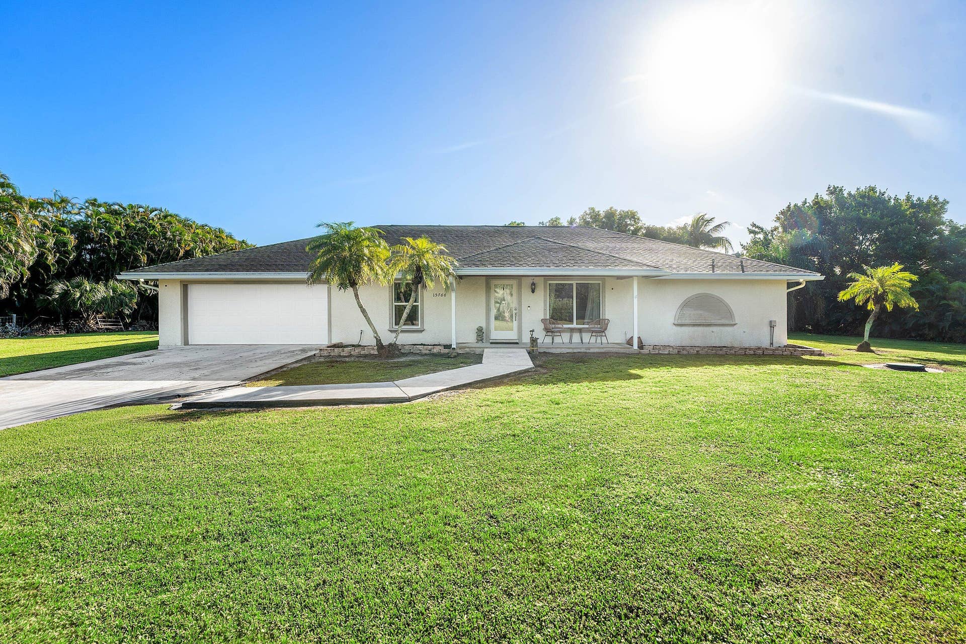 Single-story ranch exterior featuring a stucco facade, hipped tile roof, two-car garage, and a concrete walkway