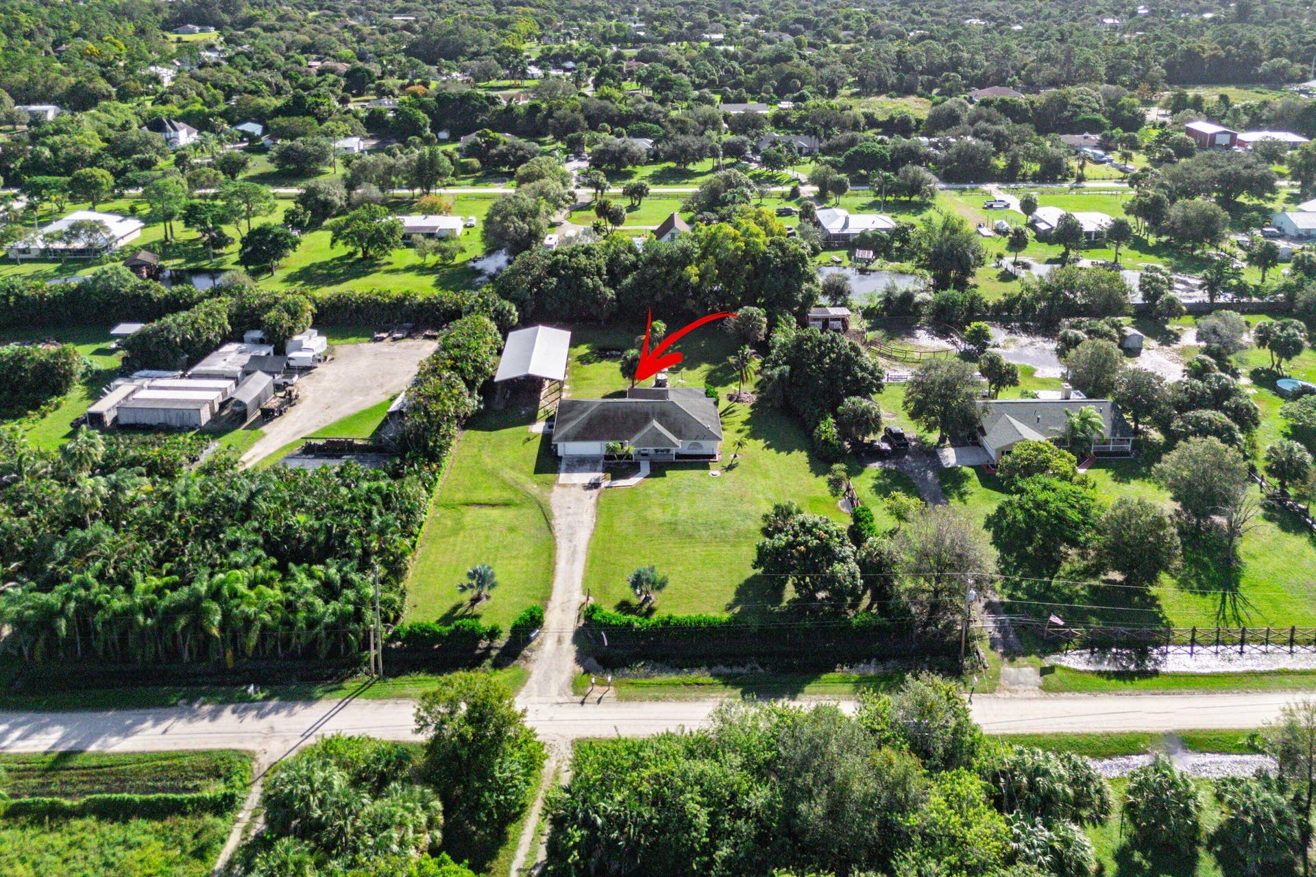 Aerial perspective of a detached residence featuring a long private driveway, an expansive manicured lawn, and an auxiliary storage structure situated on a tree-lined lot