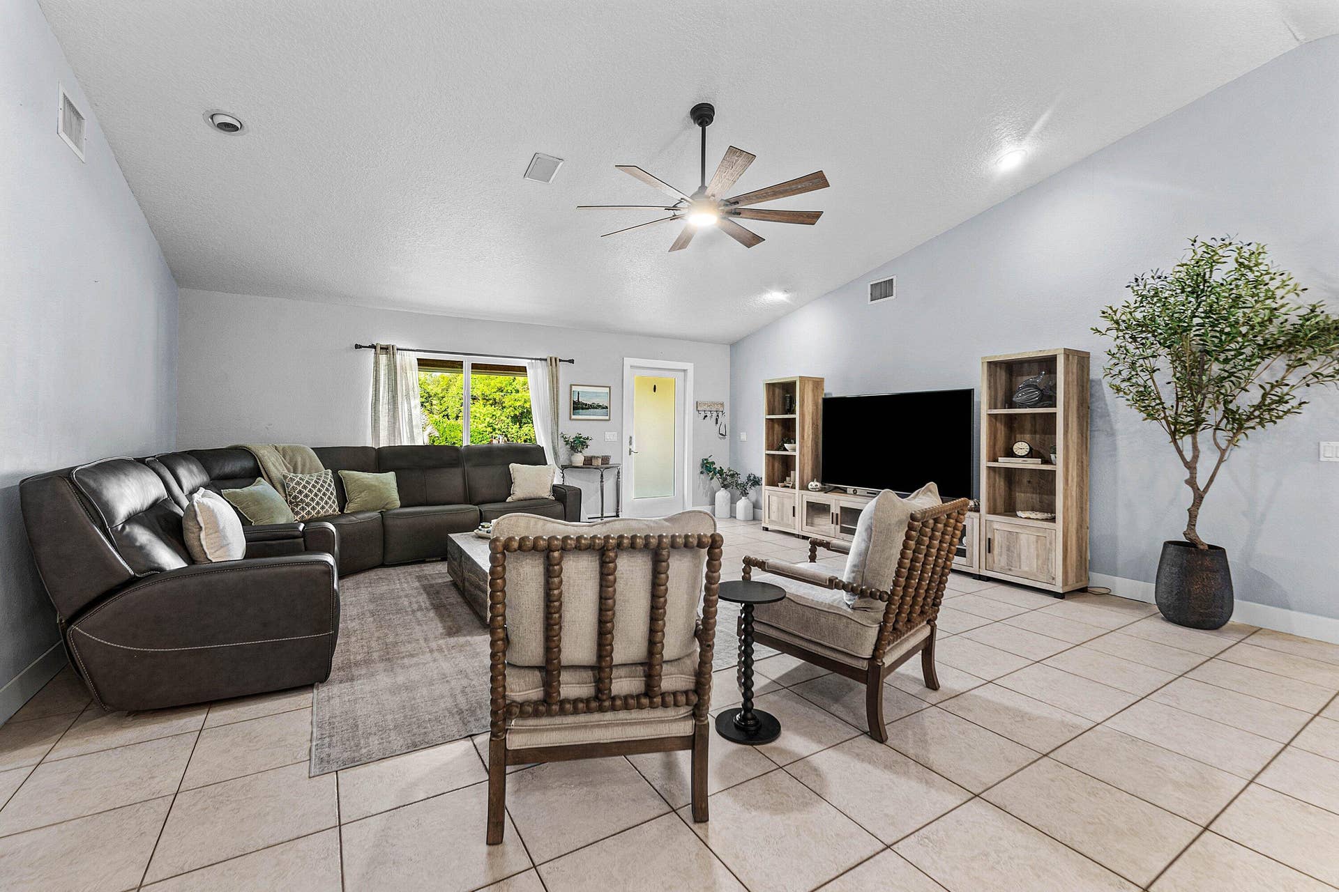 Living area featuring vaulted ceilings, neutral ceramic tile flooring, and a multi-blade ceiling fan