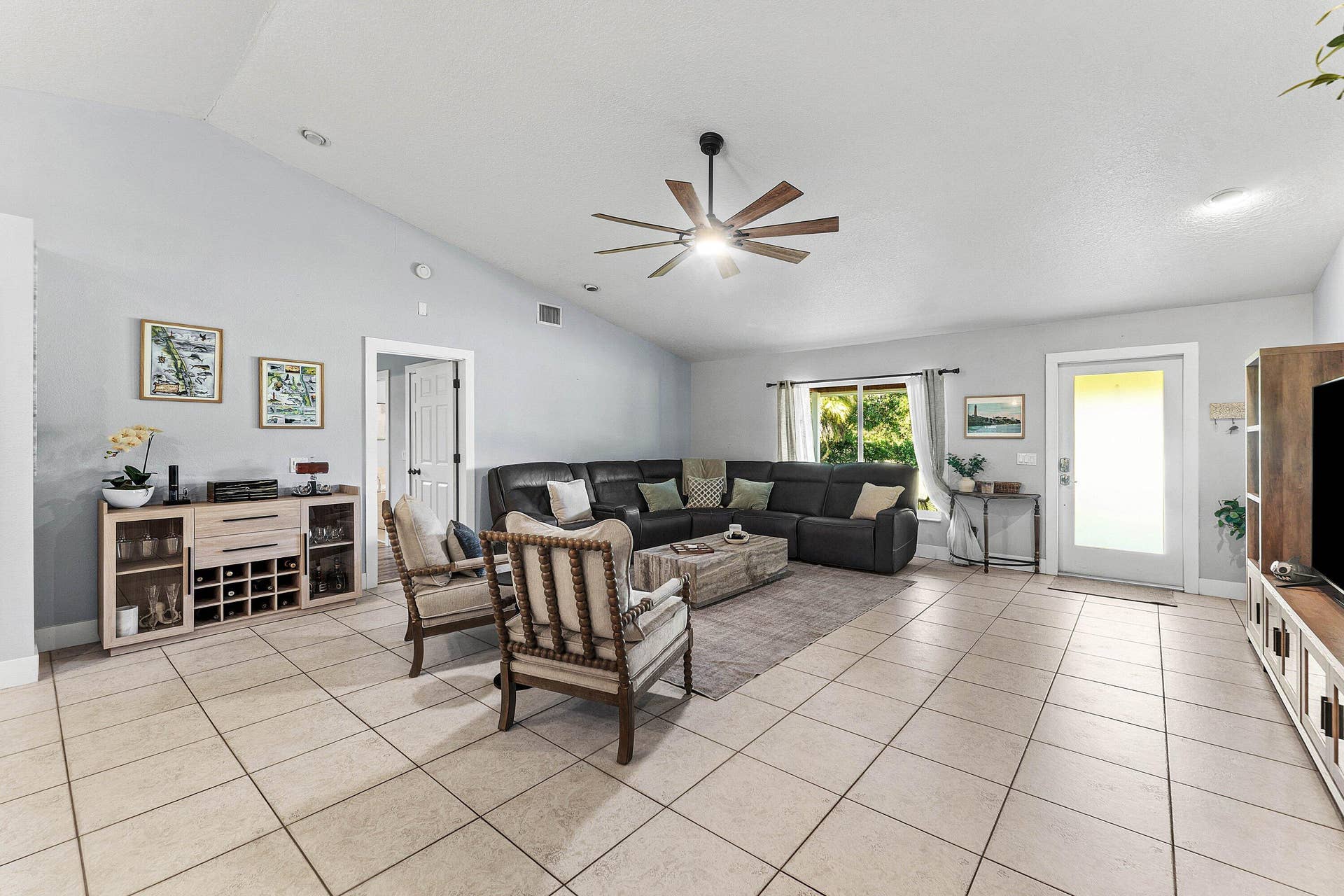 Living area featuring vaulted ceilings, large-format tile flooring, a multi-blade ceiling fan, and a glass-panel entry door