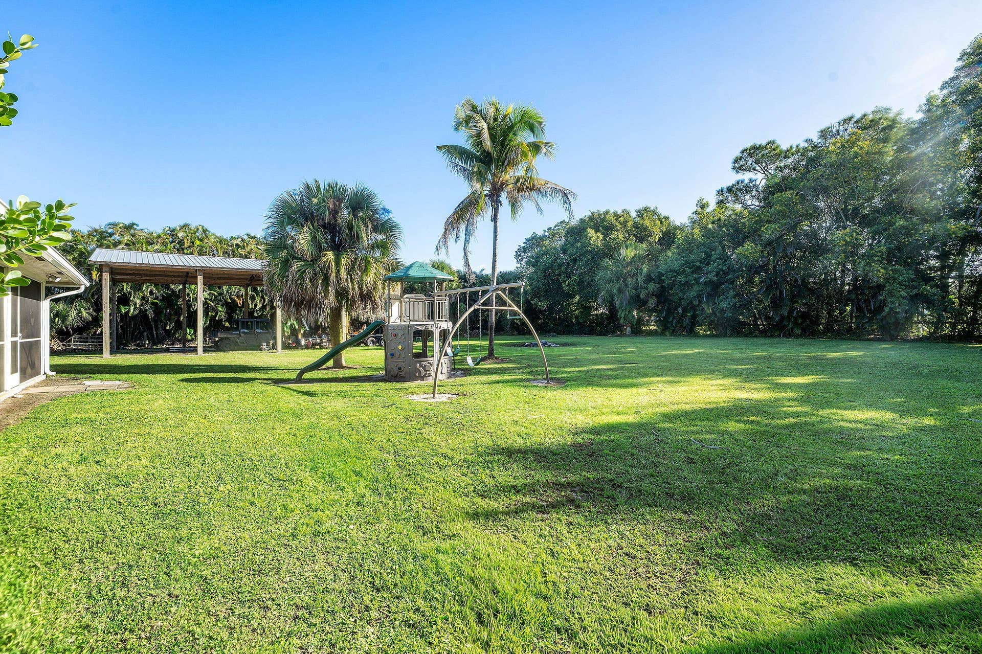 Expansive backyard featuring a large grass lawn, mature trees, and a covered patio structure