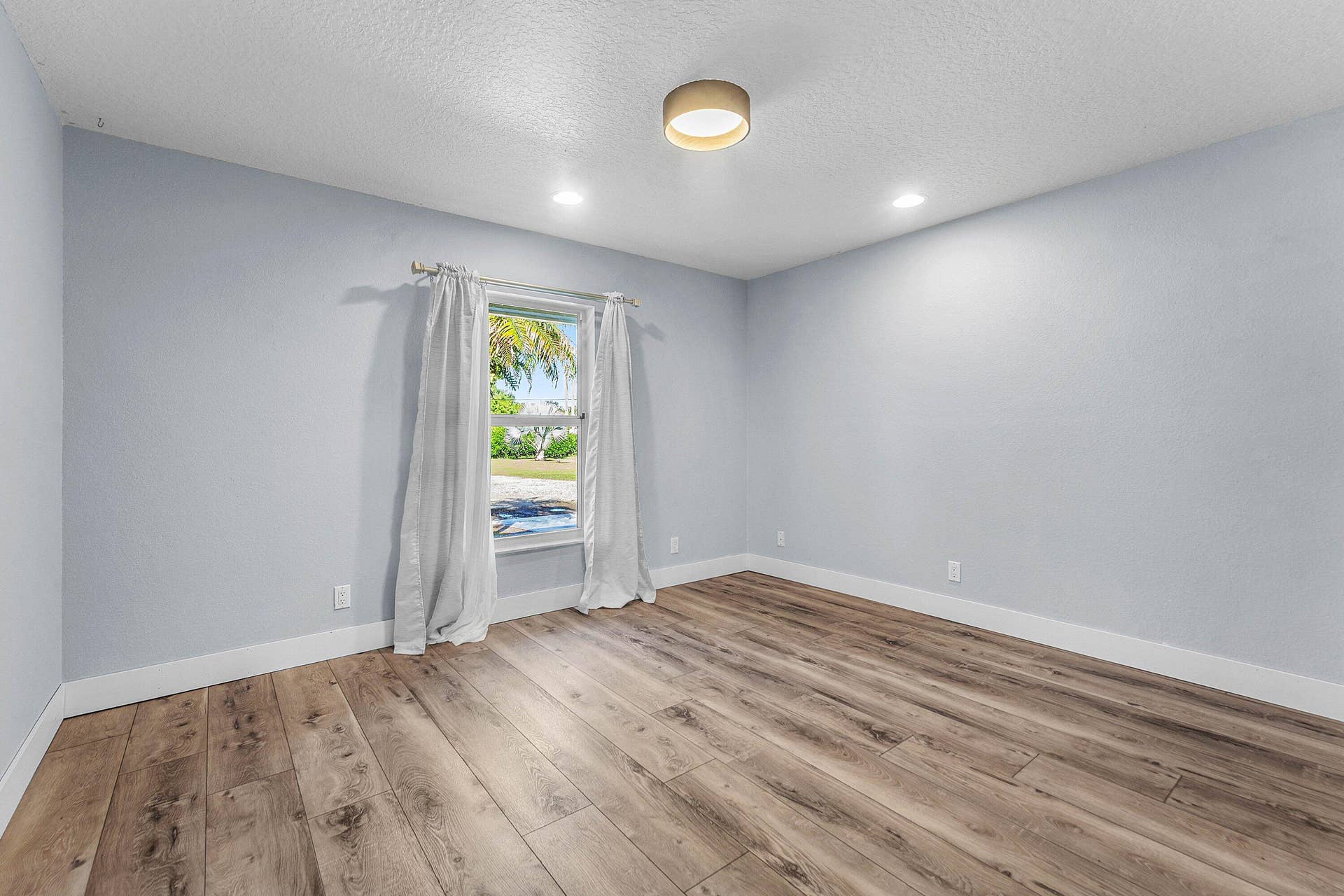 Interior room featuring wood-finish flooring, neutral wall tones, a single window, and a drum-style ceiling light fixture