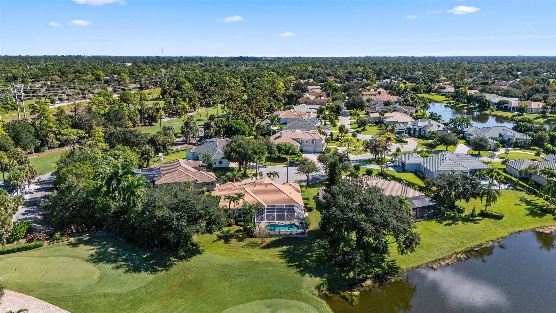Aerial perspective of a property featuring a screened-in swimming pool, tile roof, and manicured landscaping, situated directly on a golf course fairway with water frontage