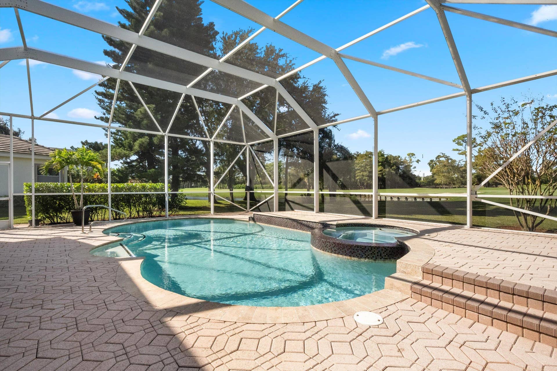Screen-enclosed pool area featuring a spillover spa, tiled deck, and brick-style pavers