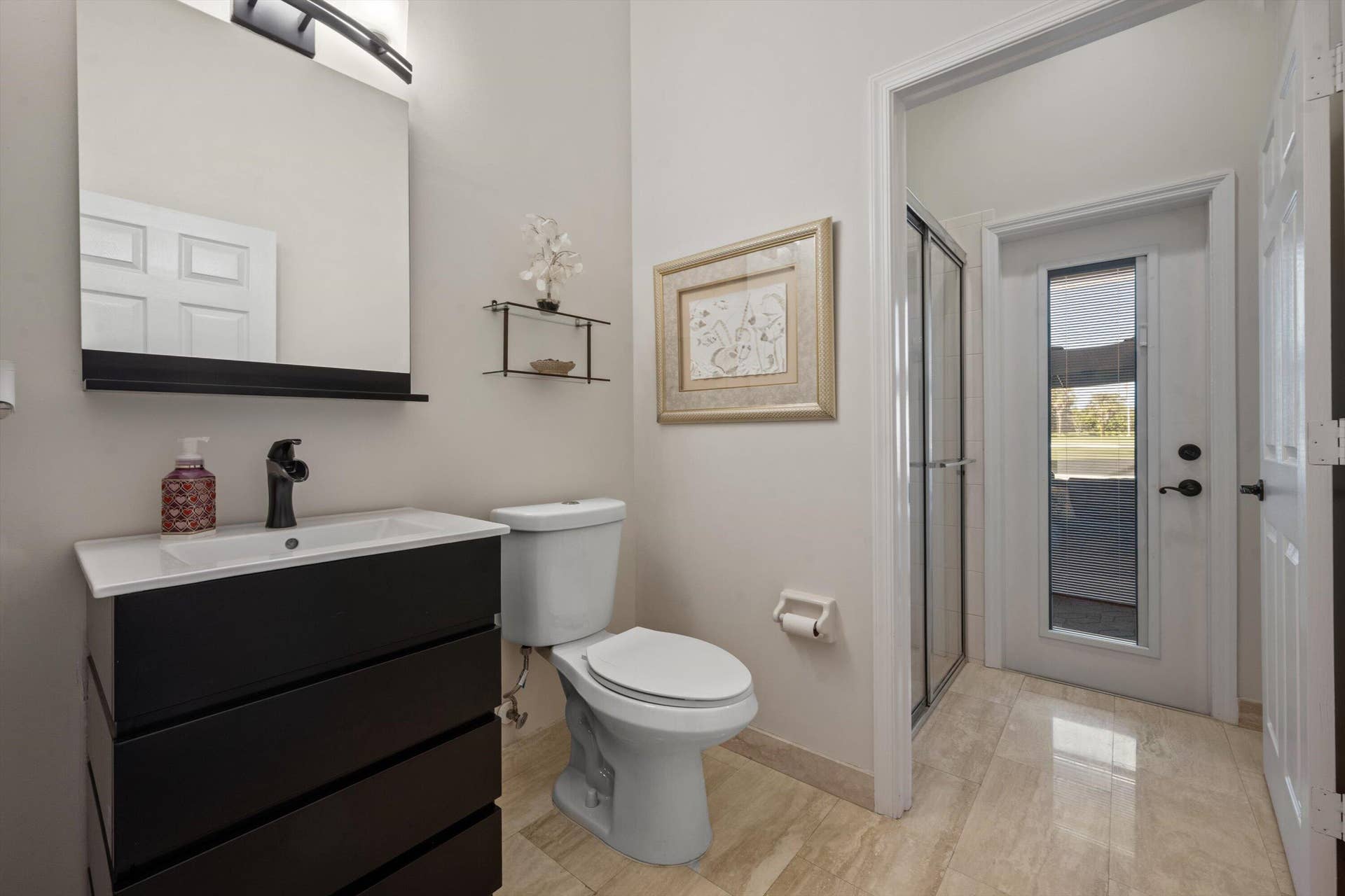 Bathroom featuring a vanity with dark-finish cabinetry, a rectangular vessel sink, and a matte black faucet, complemented by polished stone-finish flooring and a glass-enclosed shower