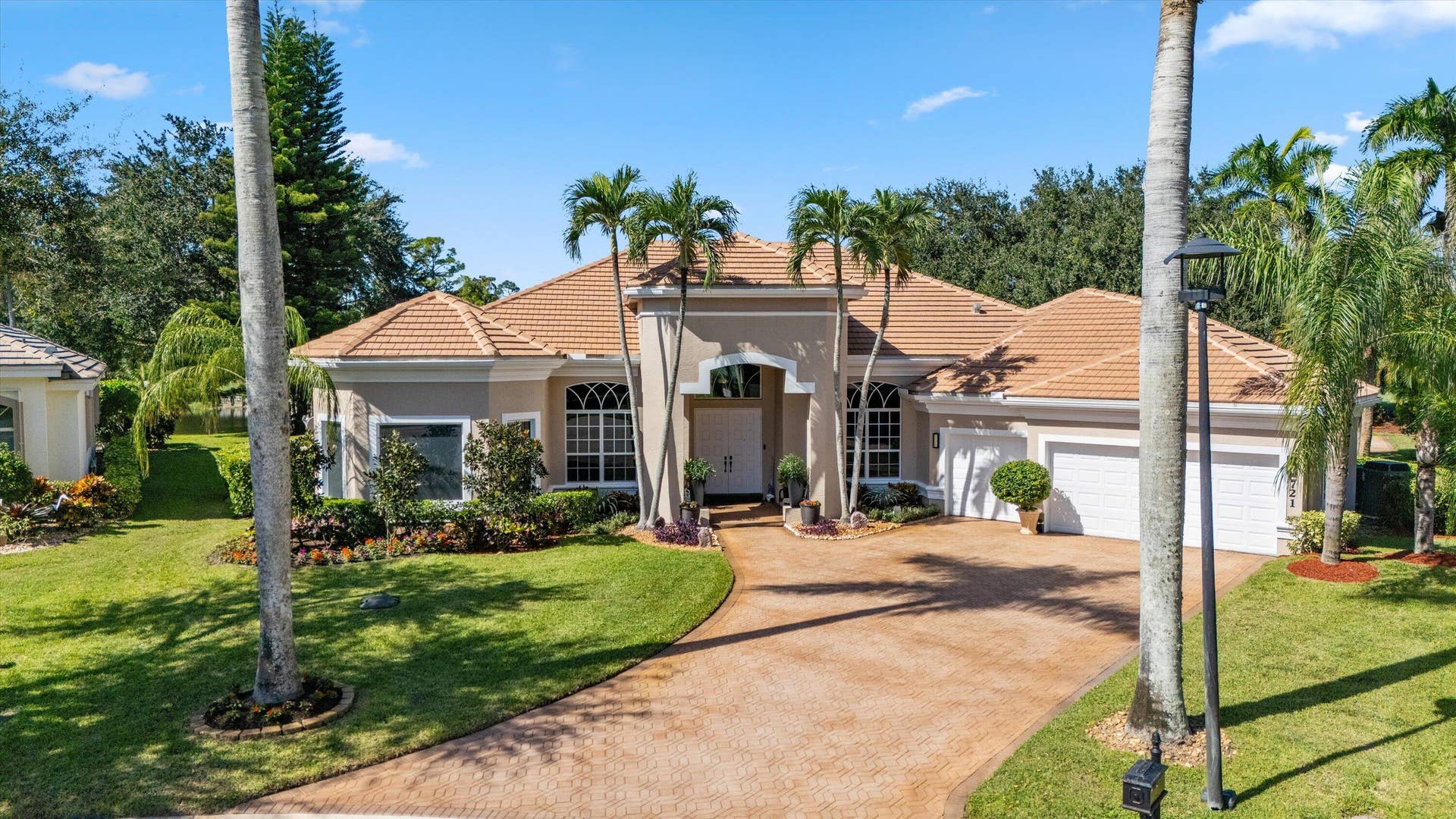 Stucco exterior featuring a clay tile roof, arched windows, grand recessed entryway, and a paver driveway leading to an attached three-car garage