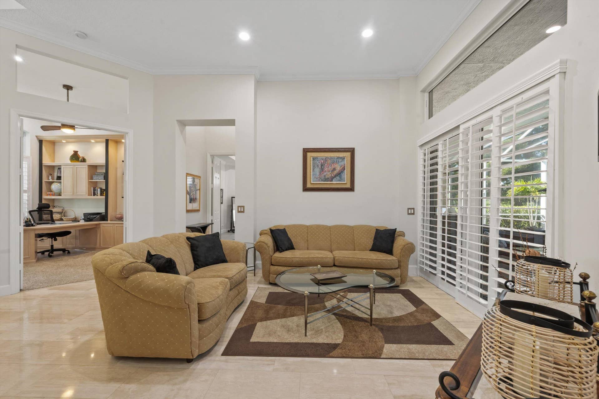 High-ceiling living area featuring neutral tile flooring, recessed lighting, and expansive sliding glass doors with plantation shutters