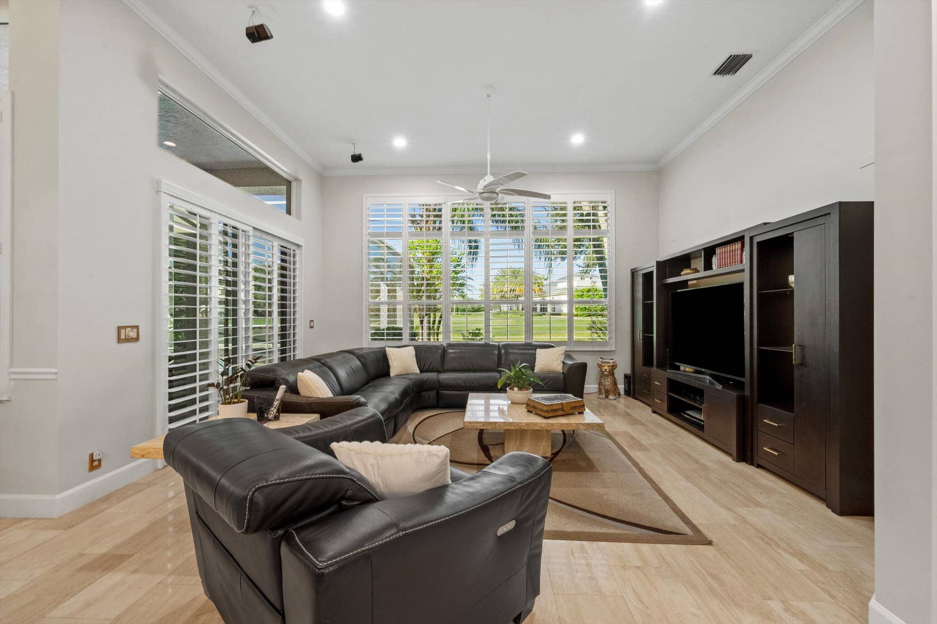 High ceilings with recessed lighting, oversized windows with plantation shutters, light-toned flooring, and built-in cabinetry