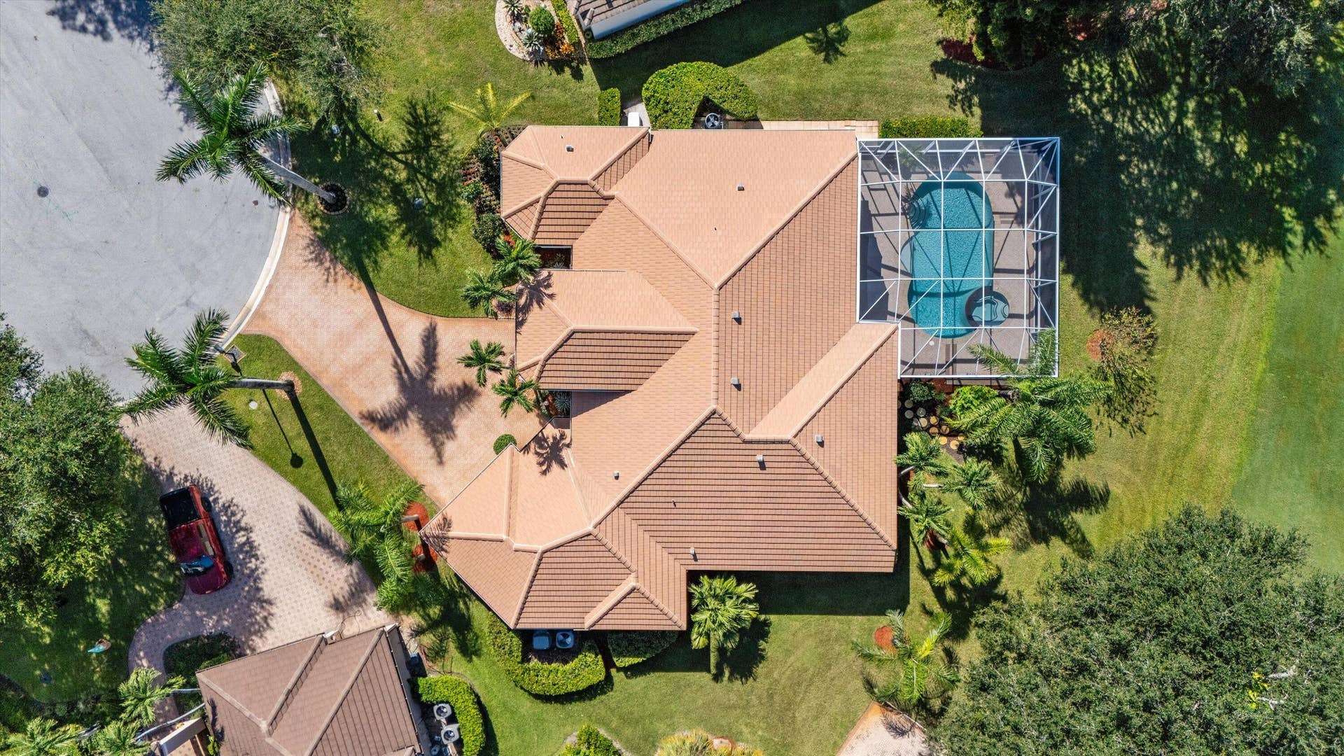 Aerial view featuring a tile roof, screened-in swimming pool with spa, paver driveway, and mature landscaping