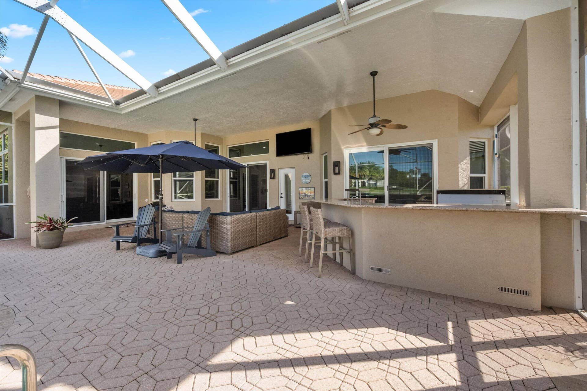 Covered lanai featuring a screen enclosure, paver flooring, built-in outdoor bar with stone countertop, and ceiling fans