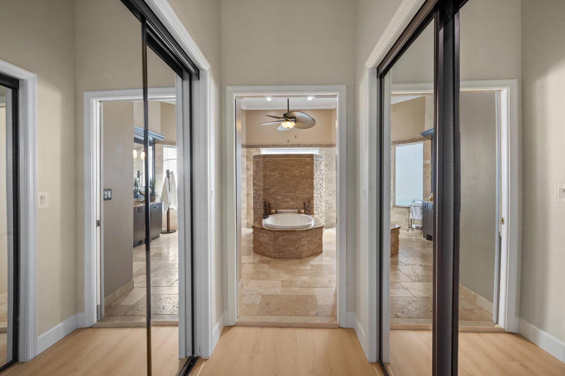 Hallway featuring dual floor-to-ceiling mirrored sliding closet doors, stone-tile flooring, and direct line-of-sight to an inset soaking tub with stone surround