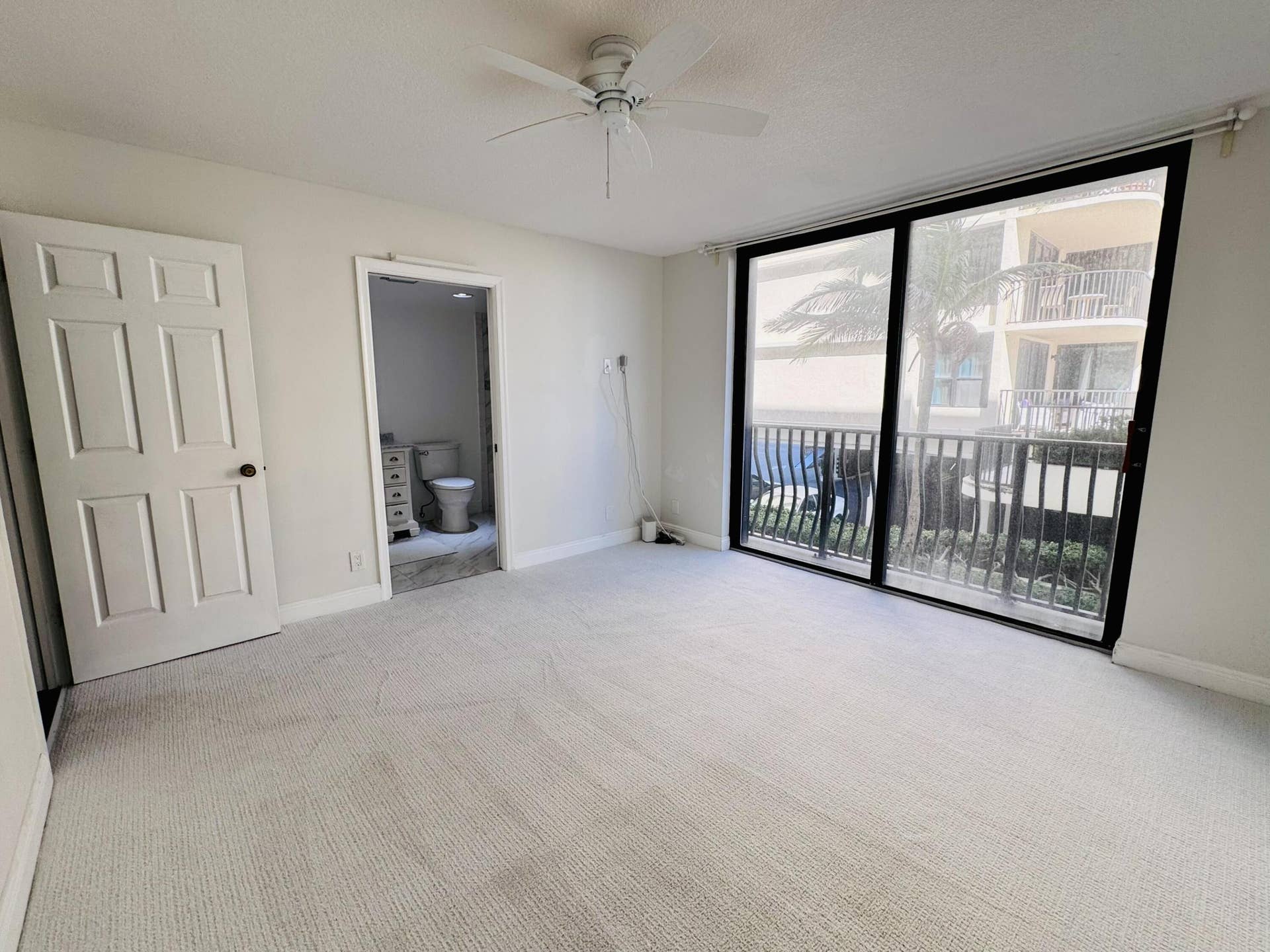 Interior space featuring neutral wall-to-wall carpeting, a ceiling fan, and floor-to-ceiling sliding glass doors with balcony access