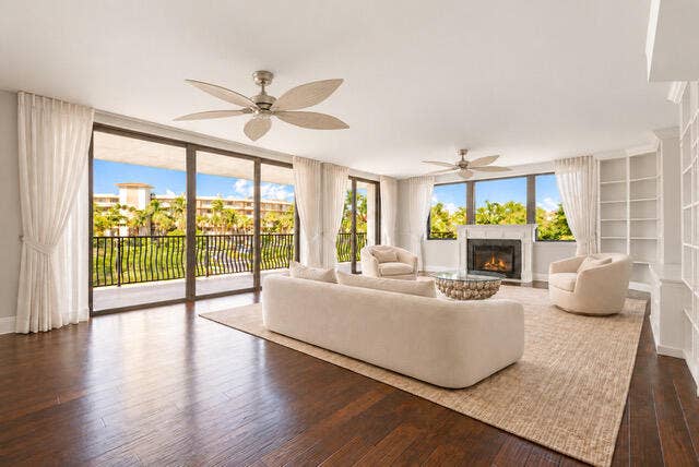 Living area featuring dark wood-finish flooring, floor-to-ceiling sliding glass doors, built-in shelving, two ceiling fans, and a fireplace with a decorative mantel