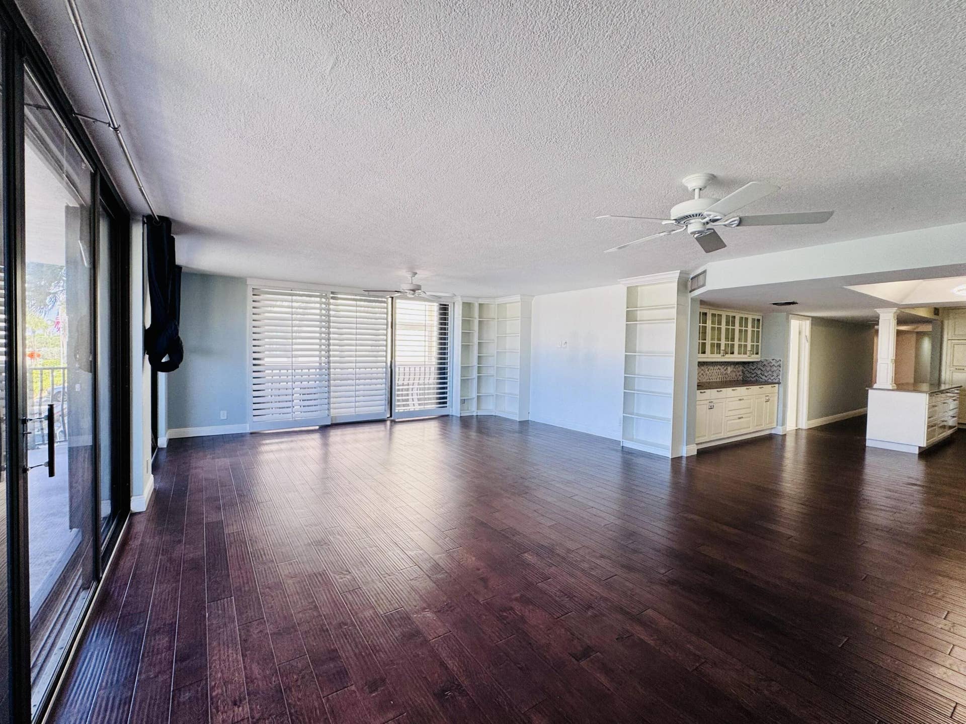 Expansive living area featuring wood-finish flooring, built-in shelving, glass sliding doors, and ceiling fans