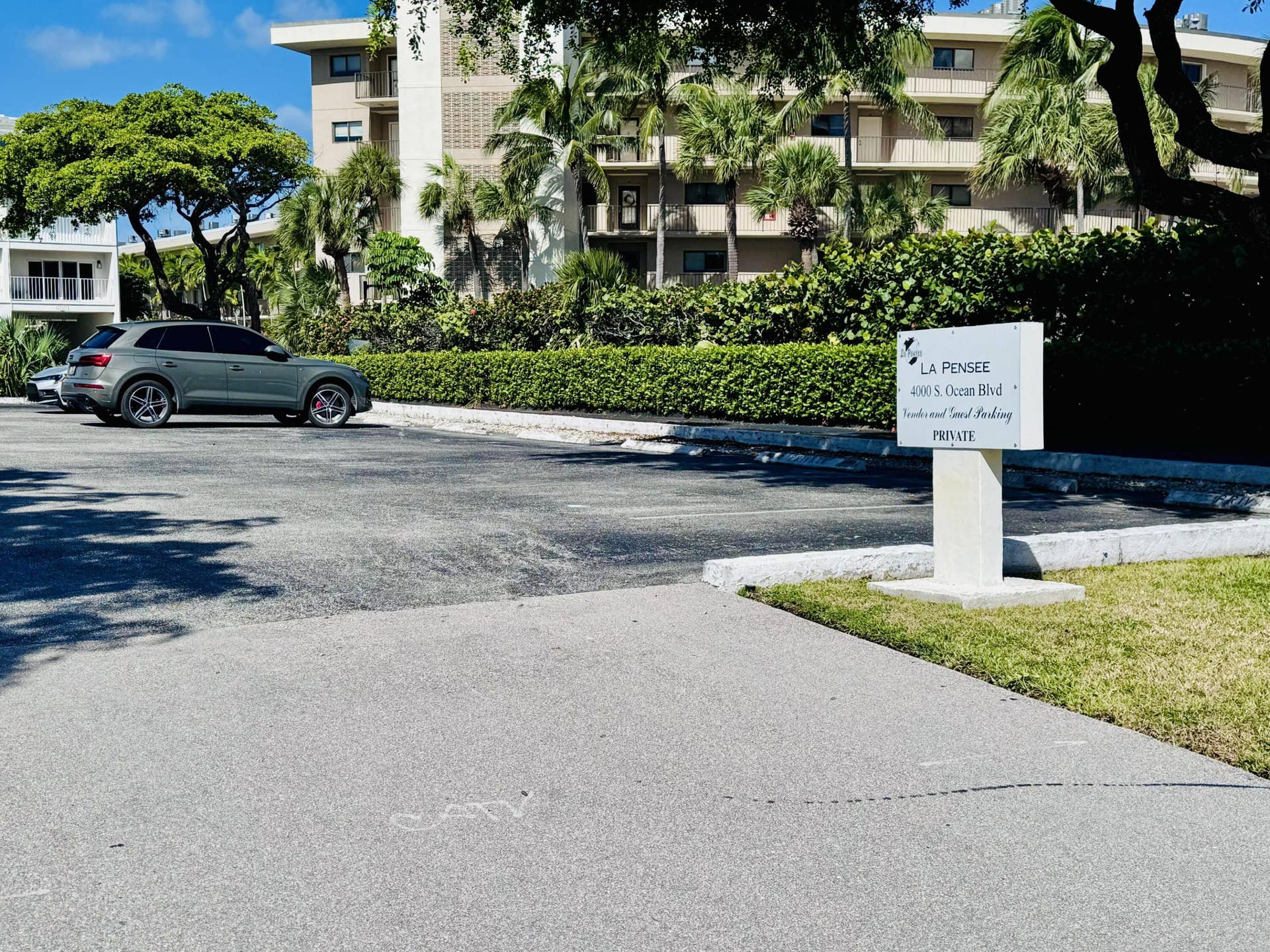 Paved surface parking area featuring perimeter landscaping with mature trees and manicured hedges