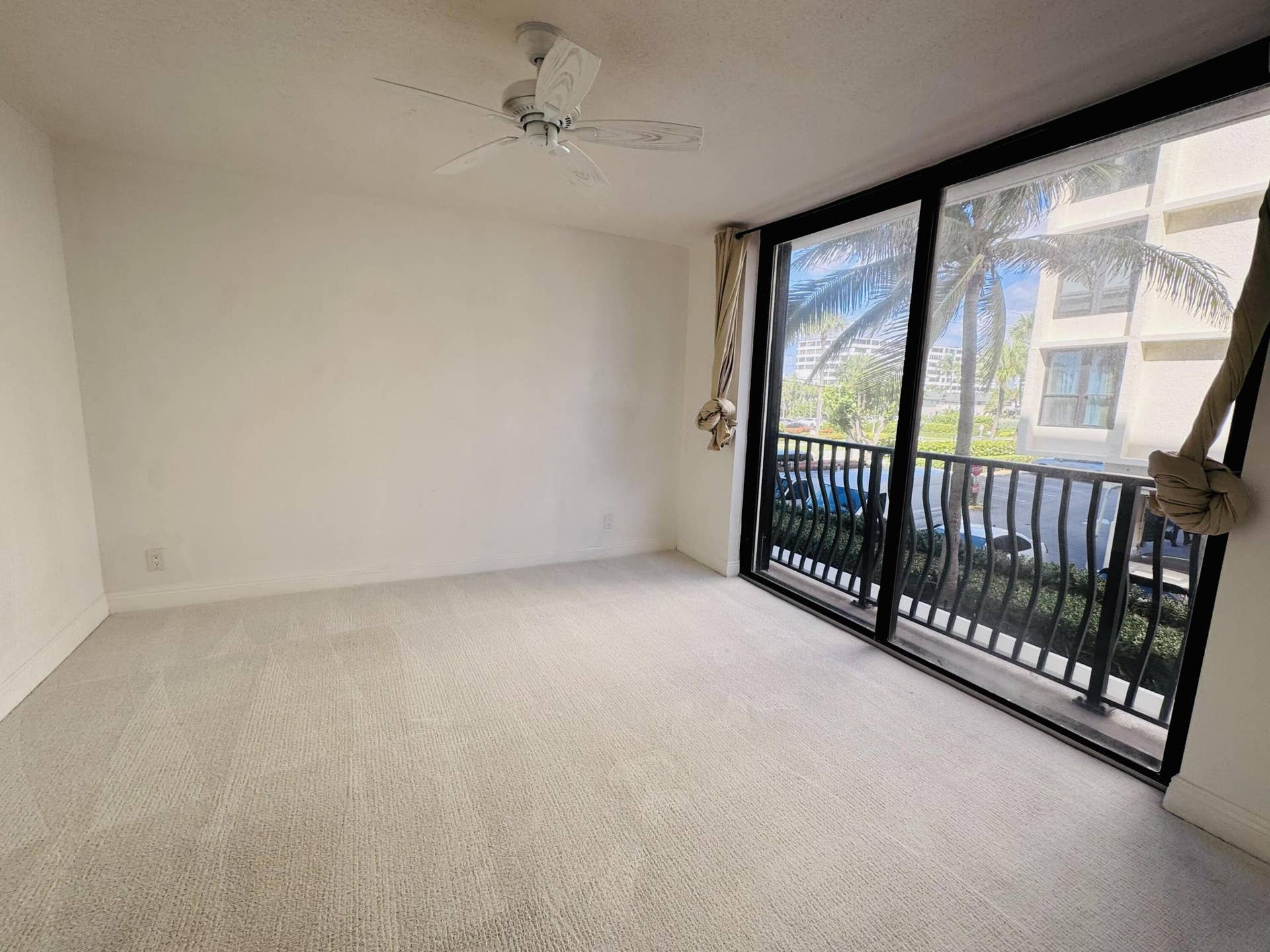Interior space featuring neutral carpeting, a ceiling fan, and floor-to-ceiling sliding glass doors opening to a balcony with black metal railings