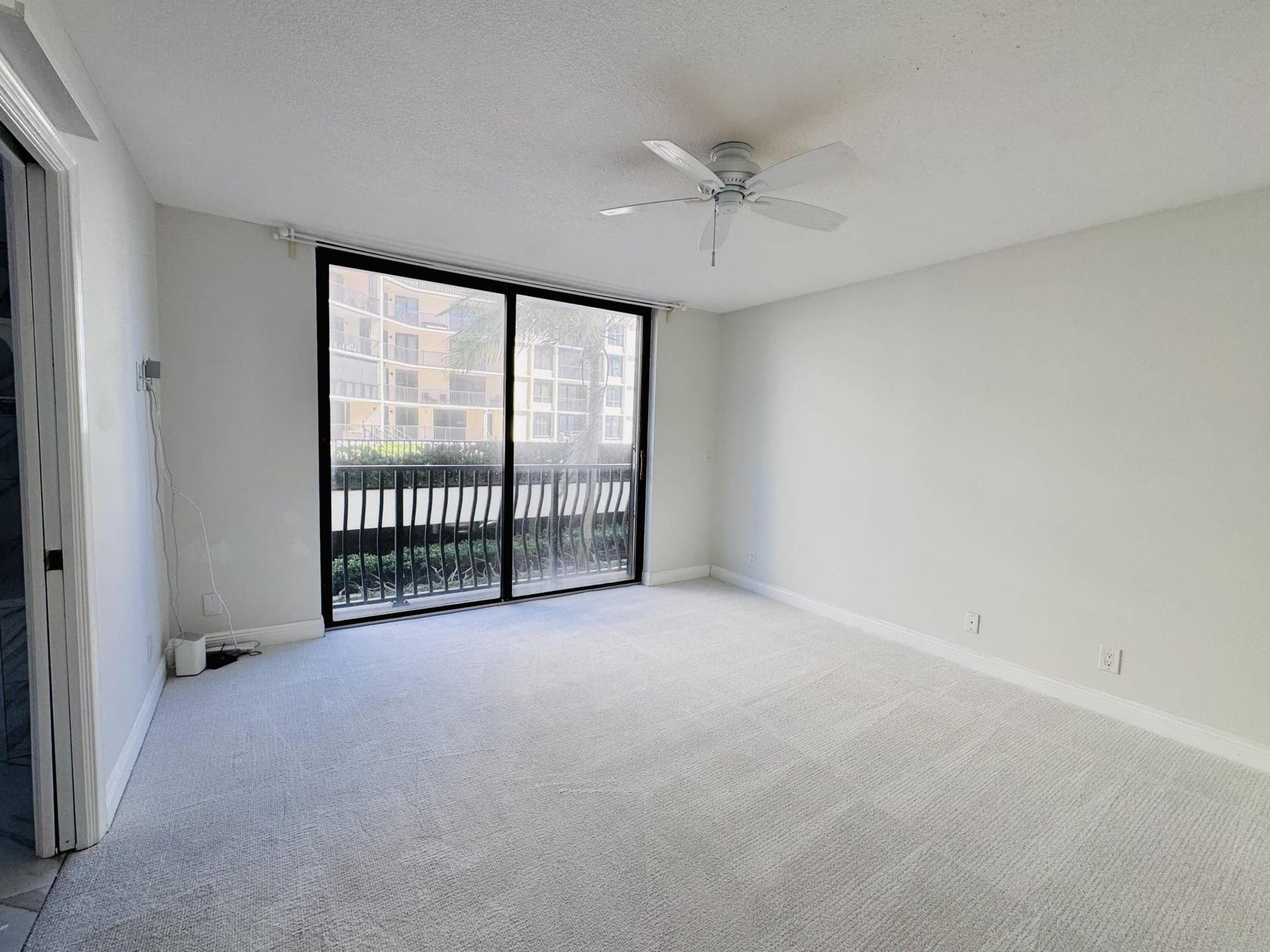 Neutral-toned carpeting, white ceiling fan with integrated lighting, and full-height sliding glass doors opening to a private balcony