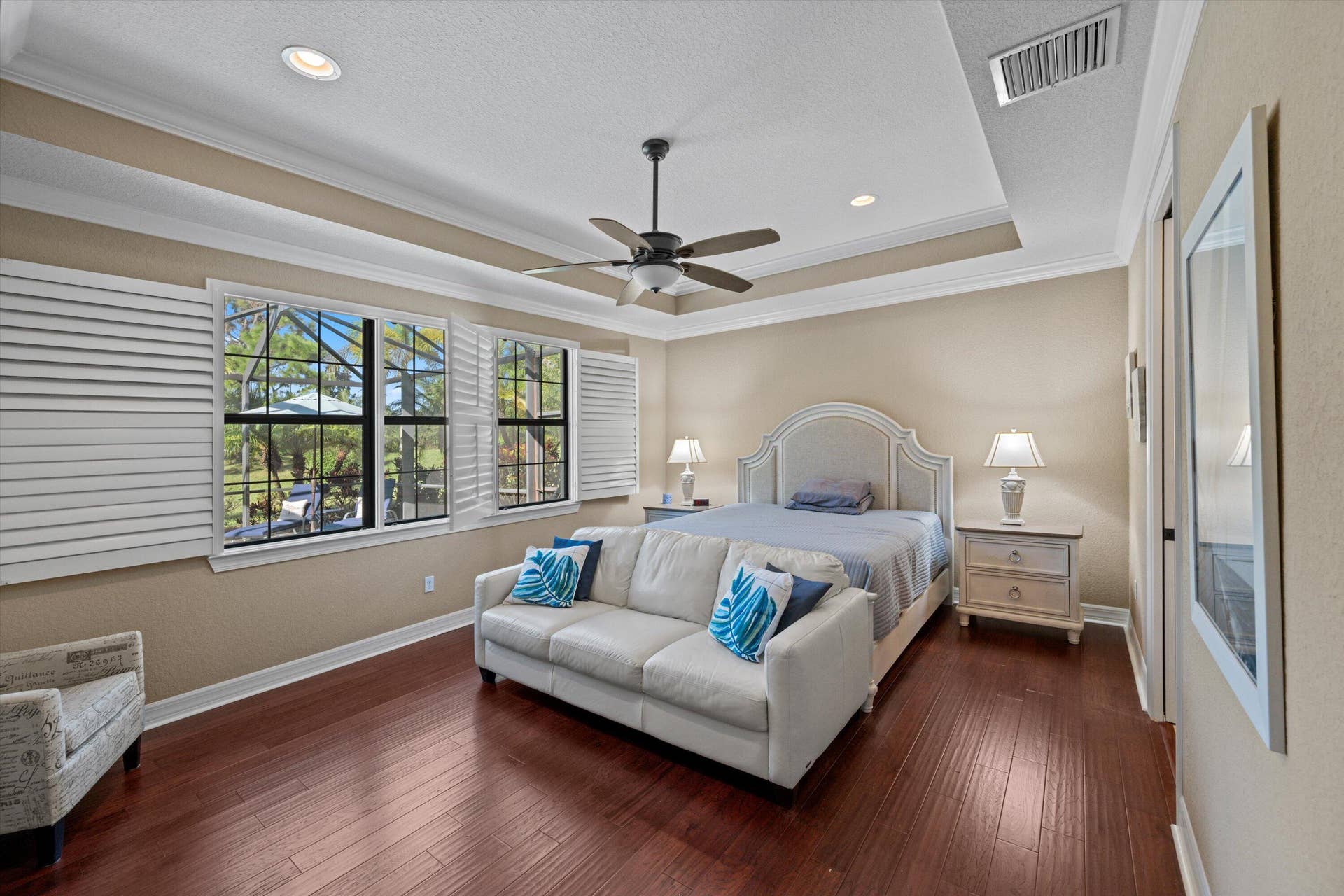 Tray ceiling featuring crown molding, dark wood-finish flooring, recessed lighting, ceiling fan, and plantation shutters