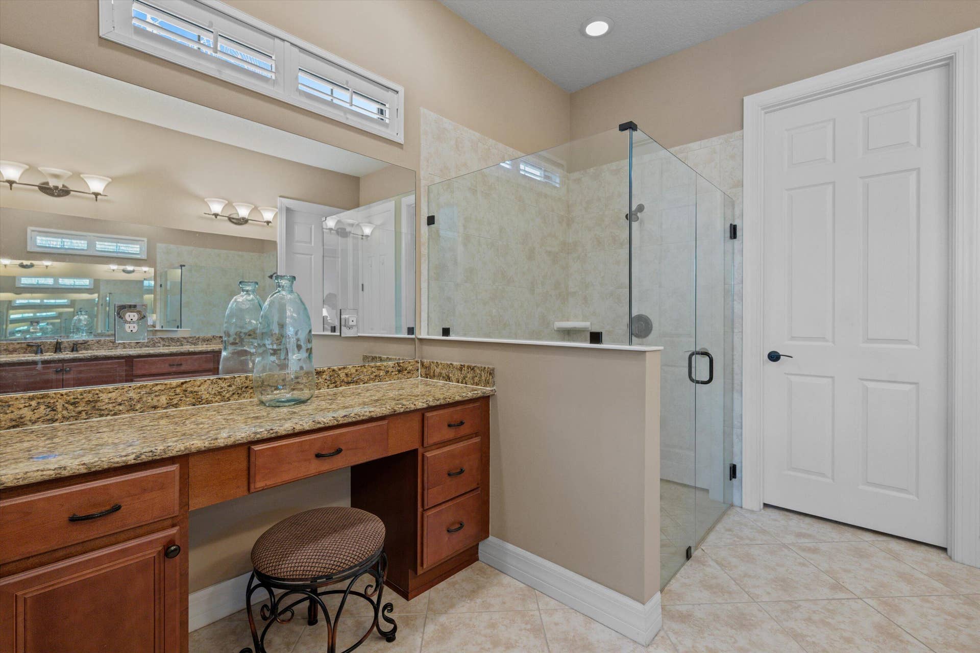 Custom cabinetry featuring a stone-look countertop, large vanity mirror with a transom window, and a walk-in shower enclosed by glass panels