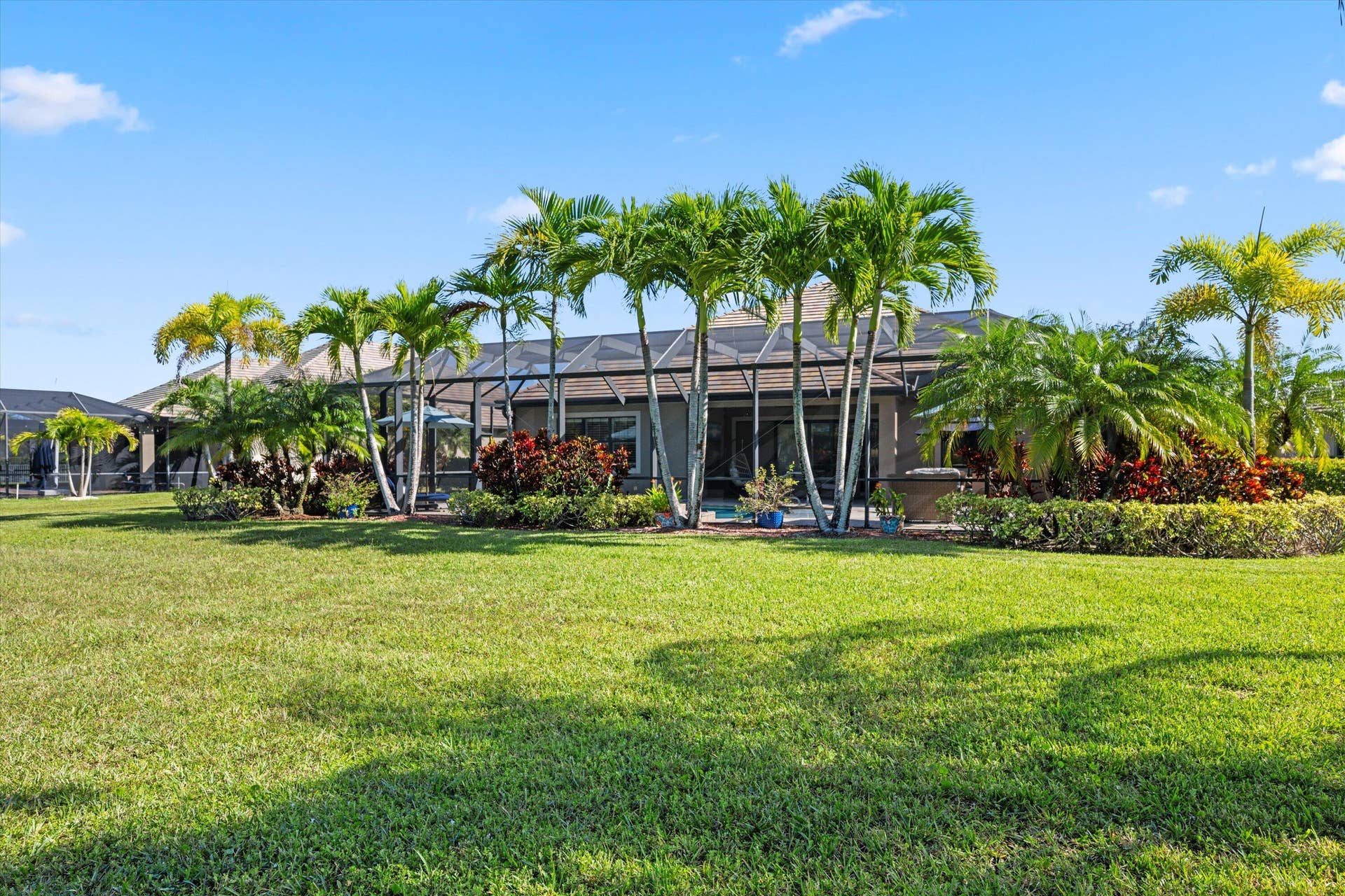 Expansive lawn featuring mature palm trees and lush perimeter landscaping, complete with a screened-in lanai