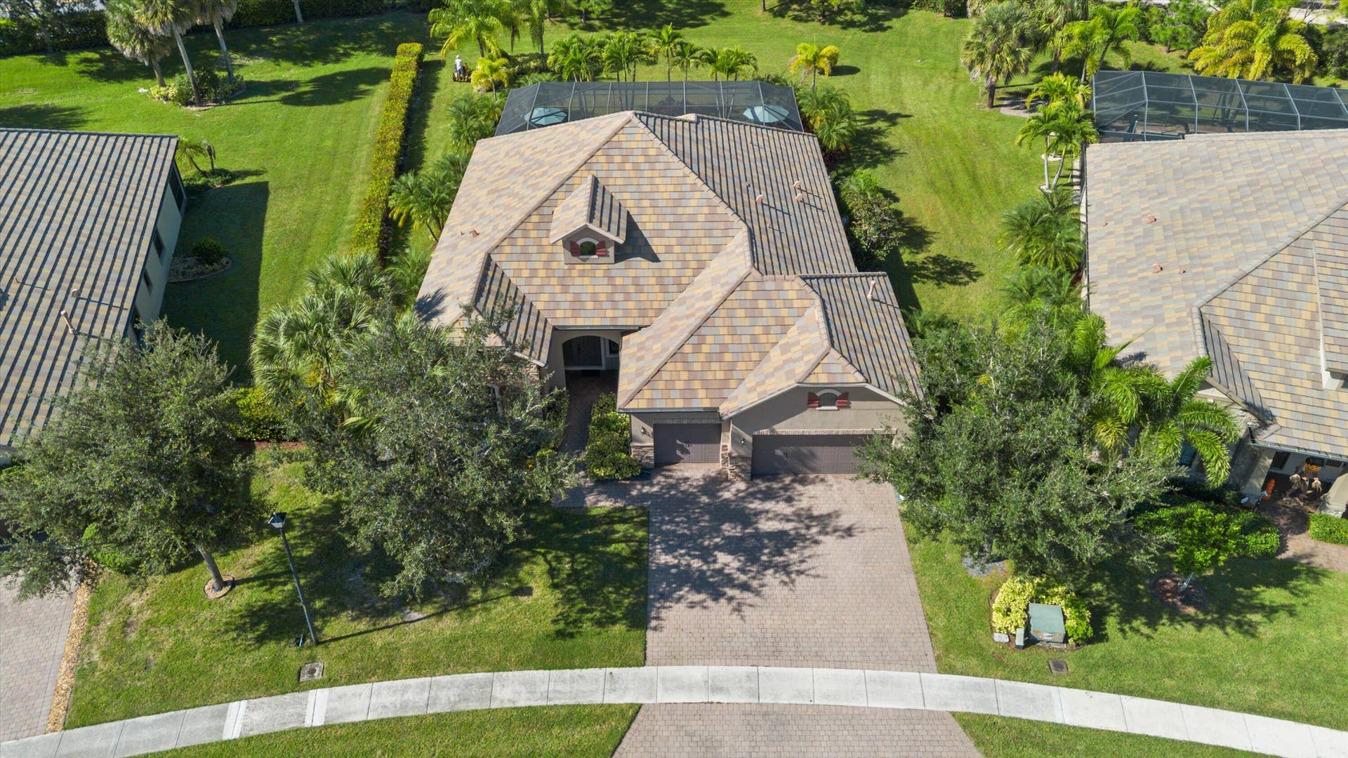 Aerial view of a residential property featuring a multi-gabled tiled roof, a screened-in rear lanai, a paved driveway, and mature landscaping