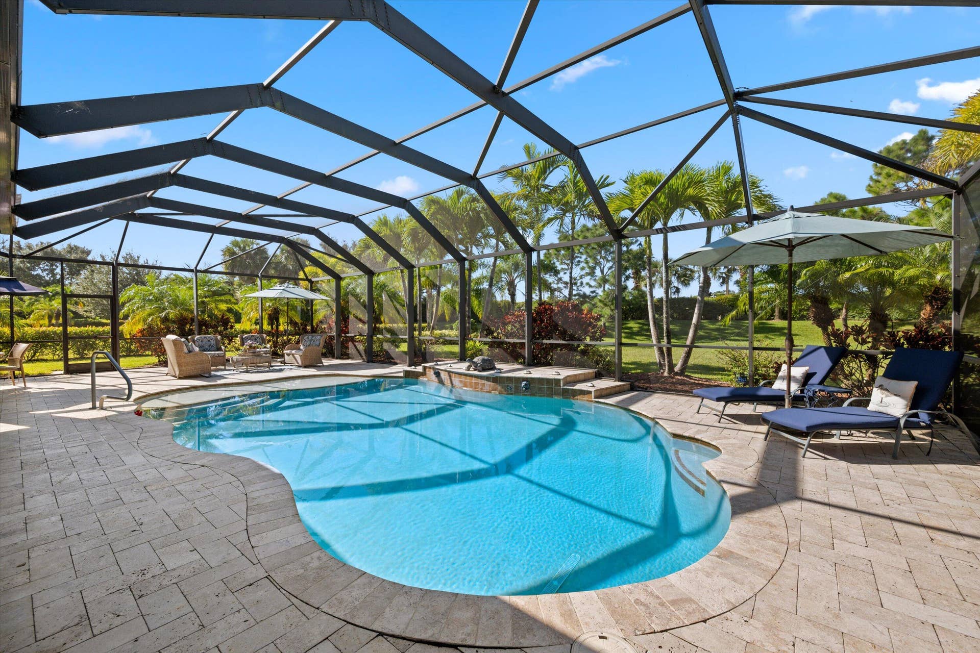 Screen-enclosed pool area featuring an in-ground pool, elevated spa, and stone-paver decking