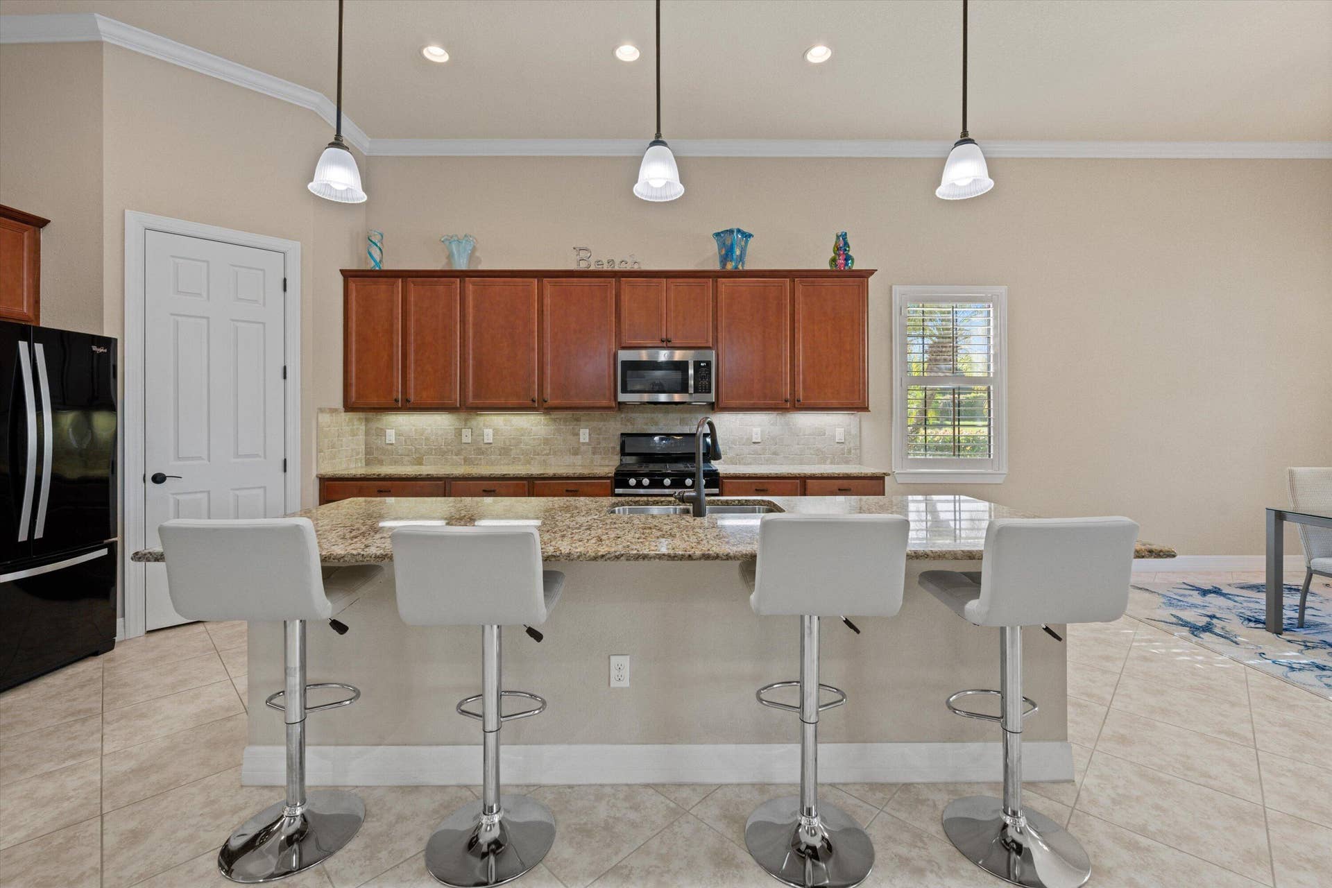 Kitchen featuring wood cabinetry, stone countertops, stainless steel appliances, a center island with bar seating, and three pendant lights