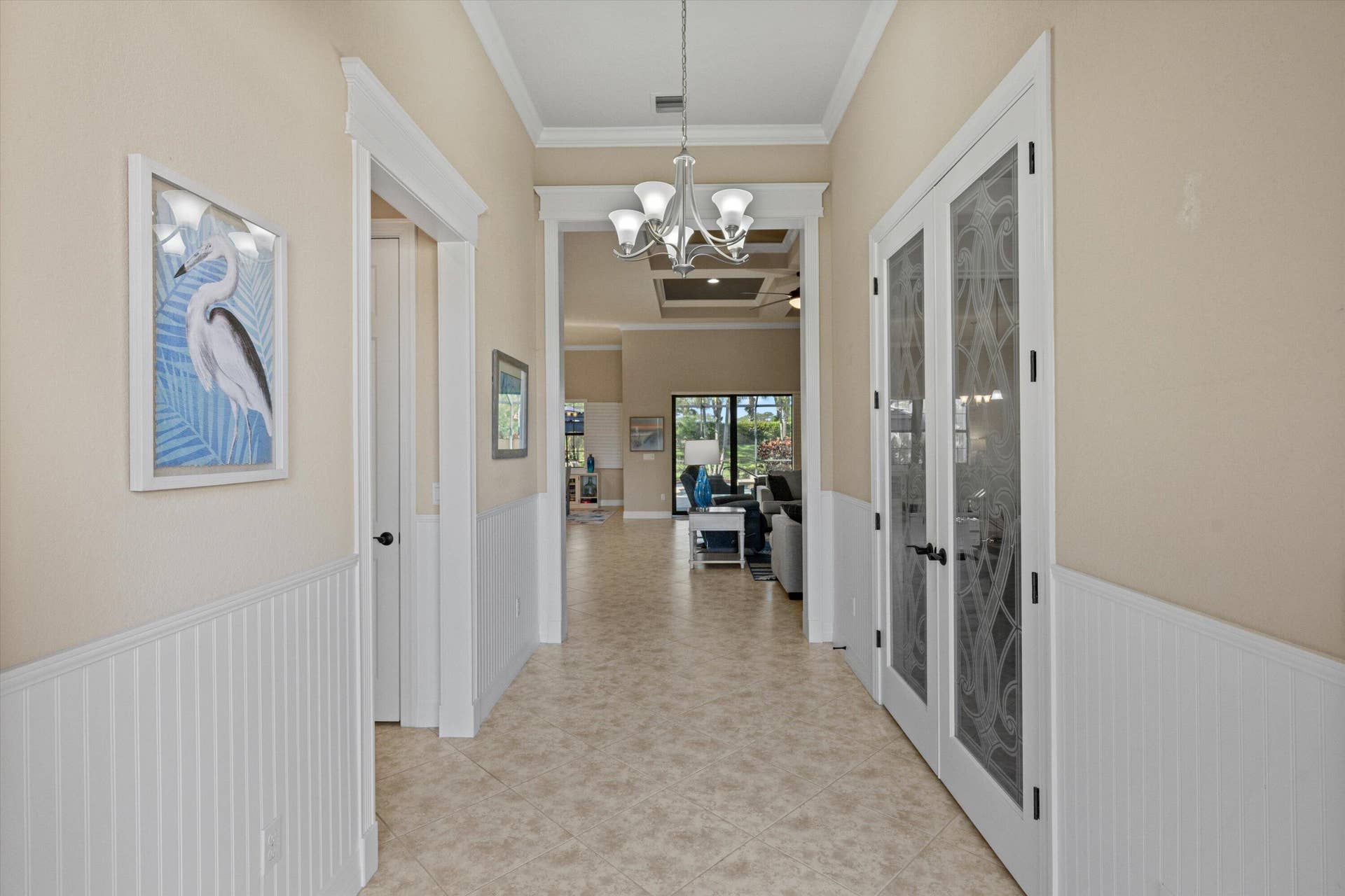 Foyer featuring white beadboard wainscoting, crown molding, tile flooring, a multi-arm chandelier, and glass-paneled French doors with decorative etched detailing