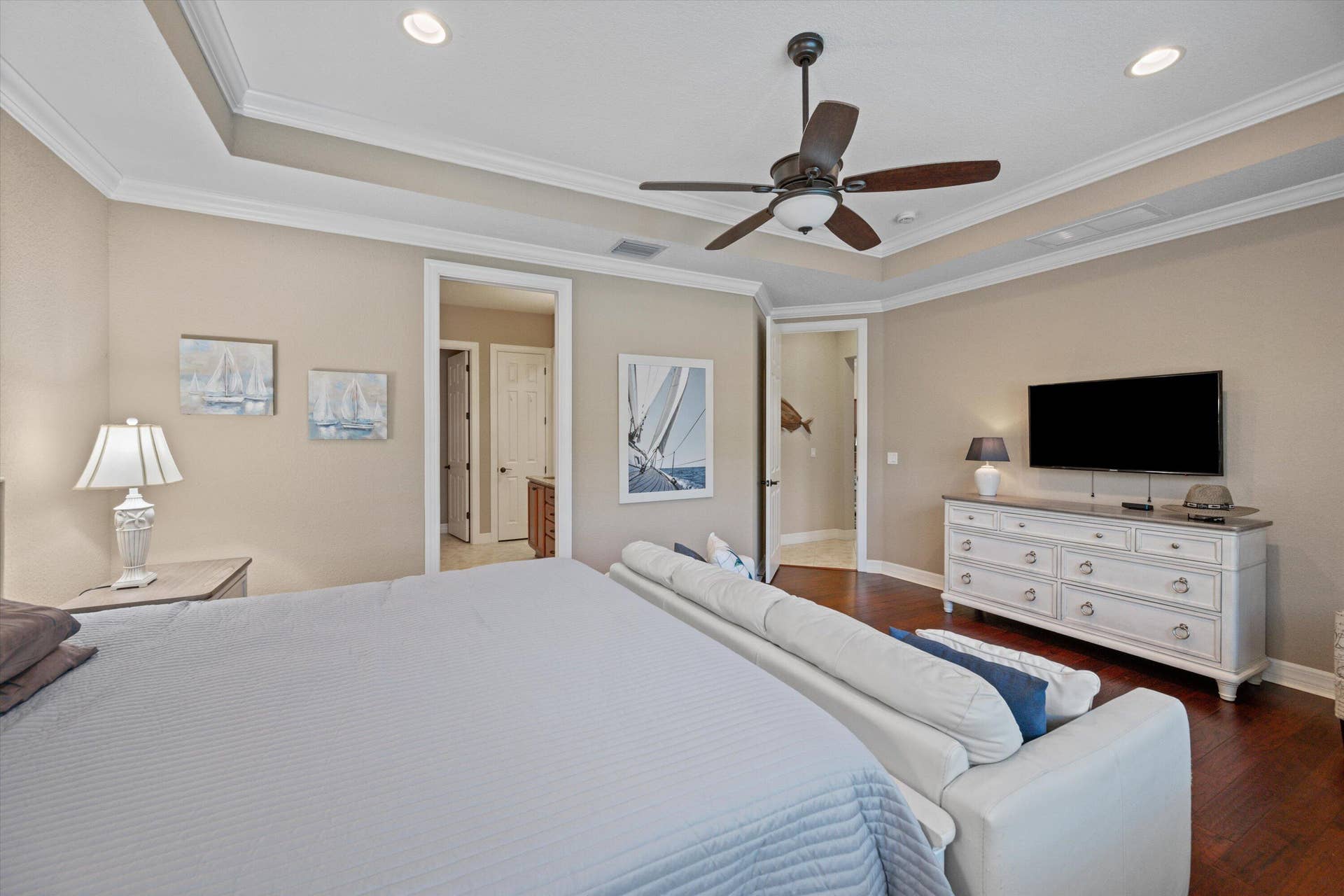 Tray ceiling featuring crown molding, recessed lighting, and ceiling fan with integrated light fixture, complemented by dark wood-finish flooring