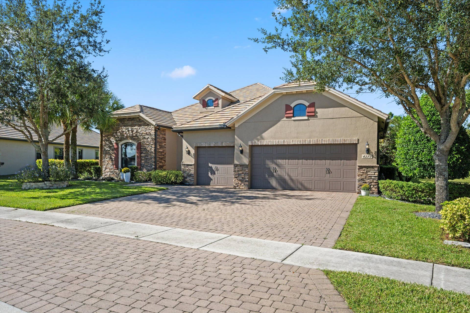 Stucco exterior featuring stone veneer accents, multi-gabled roofline, arched window detailing, three-car garage, and paved driveway