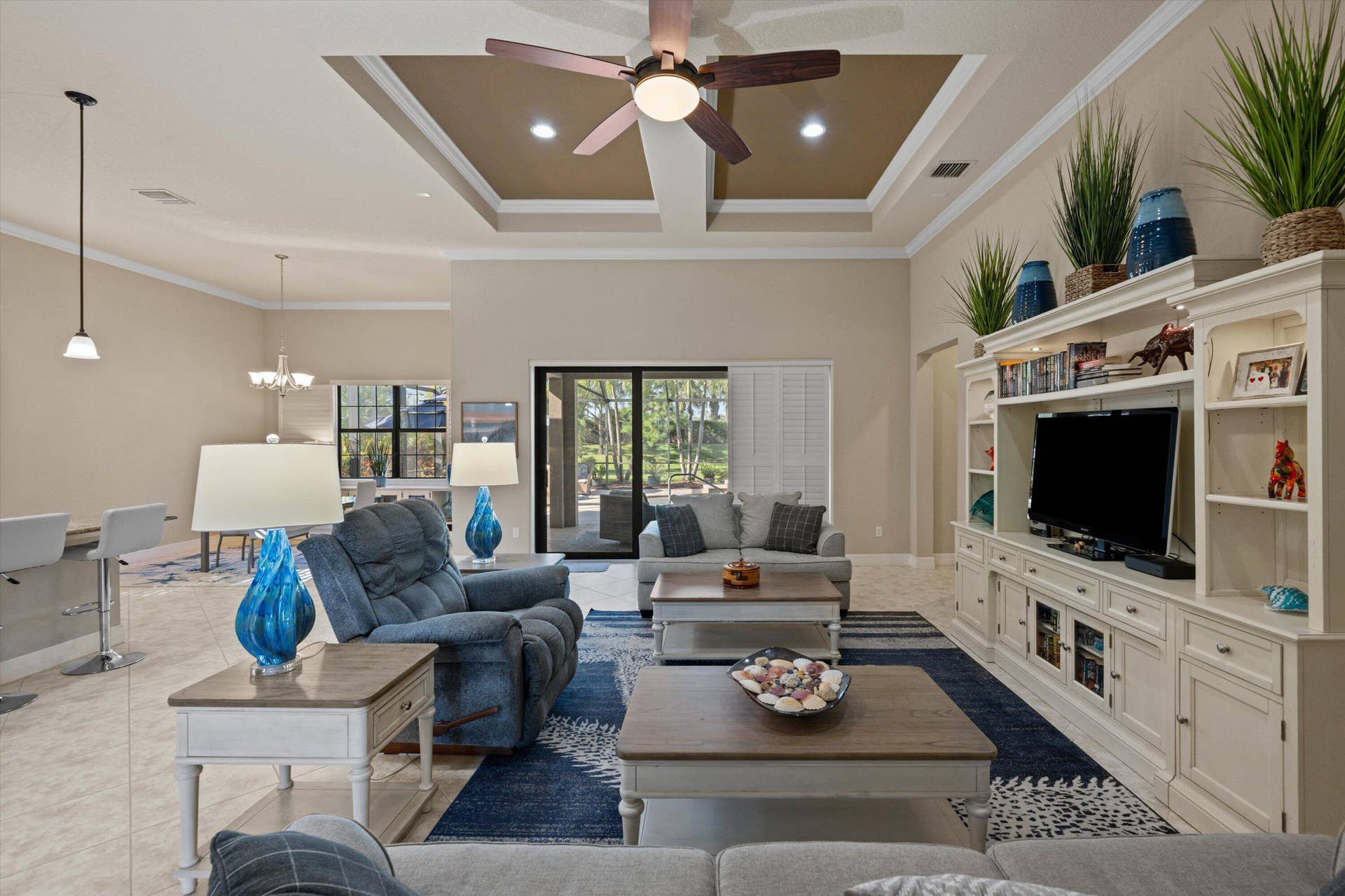 Coffered ceiling with recessed lighting, central ceiling fan, built-in floor-to-ceiling media cabinetry, tile flooring, and sliding glass doors