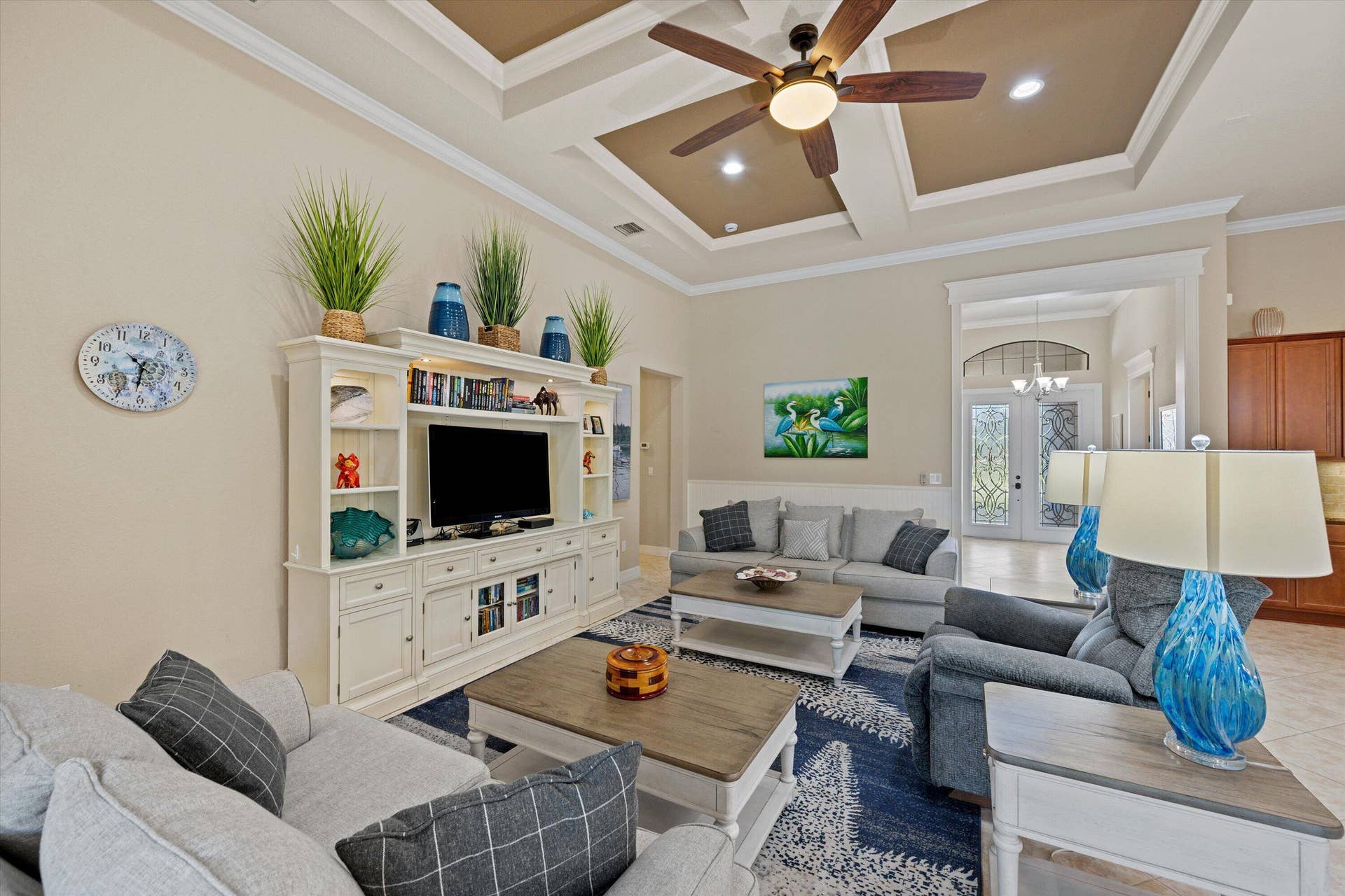 Coffered ceiling with integrated recessed lighting, central ceiling fan, built-in white cabinetry, and crown molding