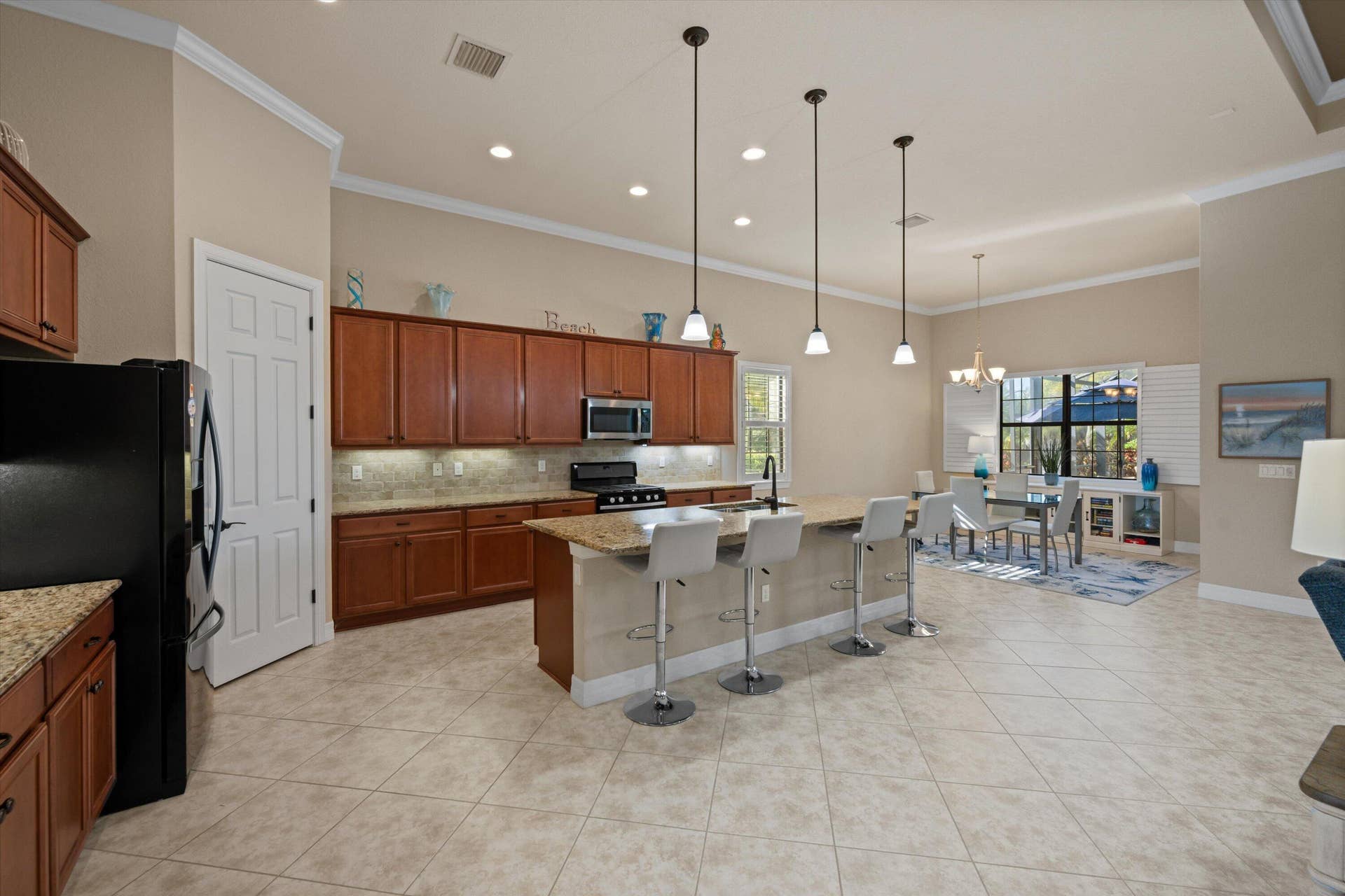 Kitchen featuring cabinetry with stained wood finish, stone-surfaced countertops, a center island with bar seating, pendant lighting, and tile flooring