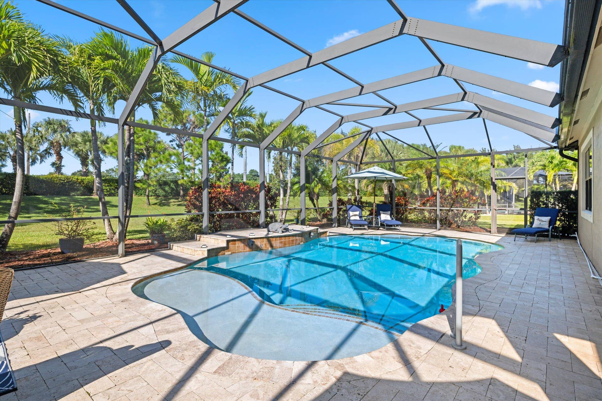 Screened-in patio featuring a paver deck, built-in swimming pool with step entry, stone-finished spillover, and surrounding palm trees