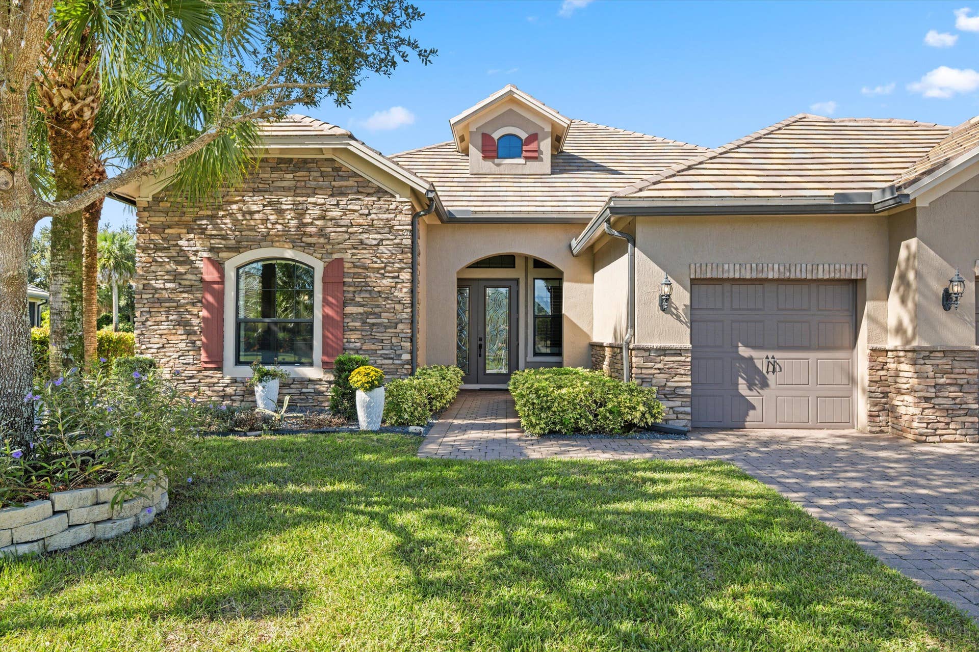 Single-story residence featuring a stone veneer and stucco facade, arched entryway, decorative shutters, and a paver driveway