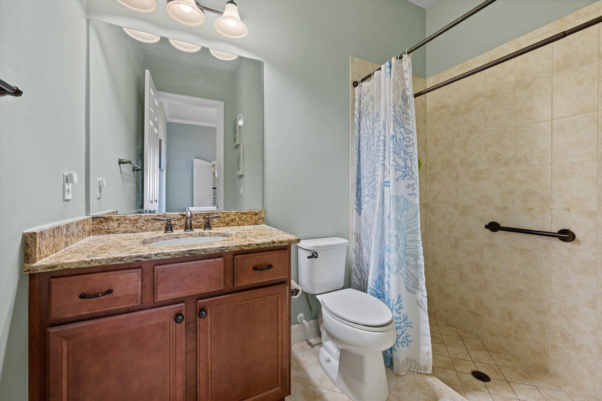 Bathroom featuring wood-finish cabinetry, stone-texture countertop, integrated sink, and walk-in shower with tile surround