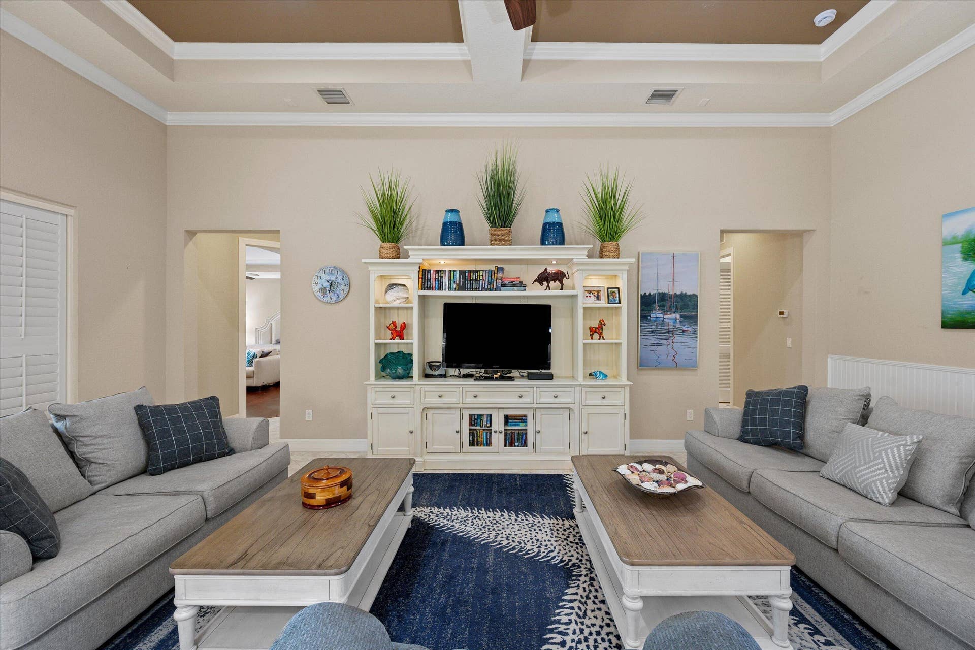 Tray ceiling with crown molding, built-in white entertainment center, and plantation shutters