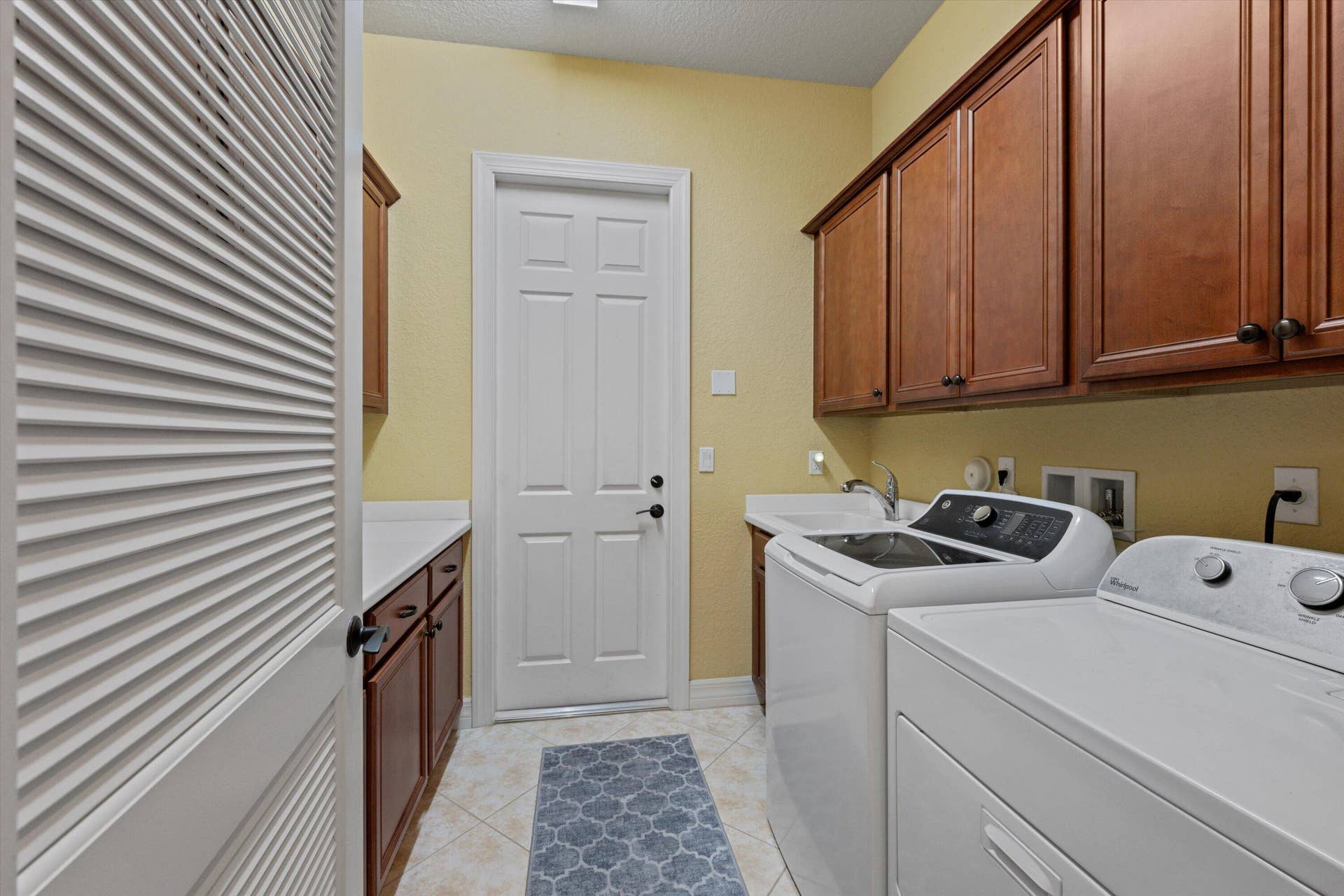 Laundry room featuring wood-finish cabinetry, solid-surface countertops, a built-in utility sink, and tile flooring