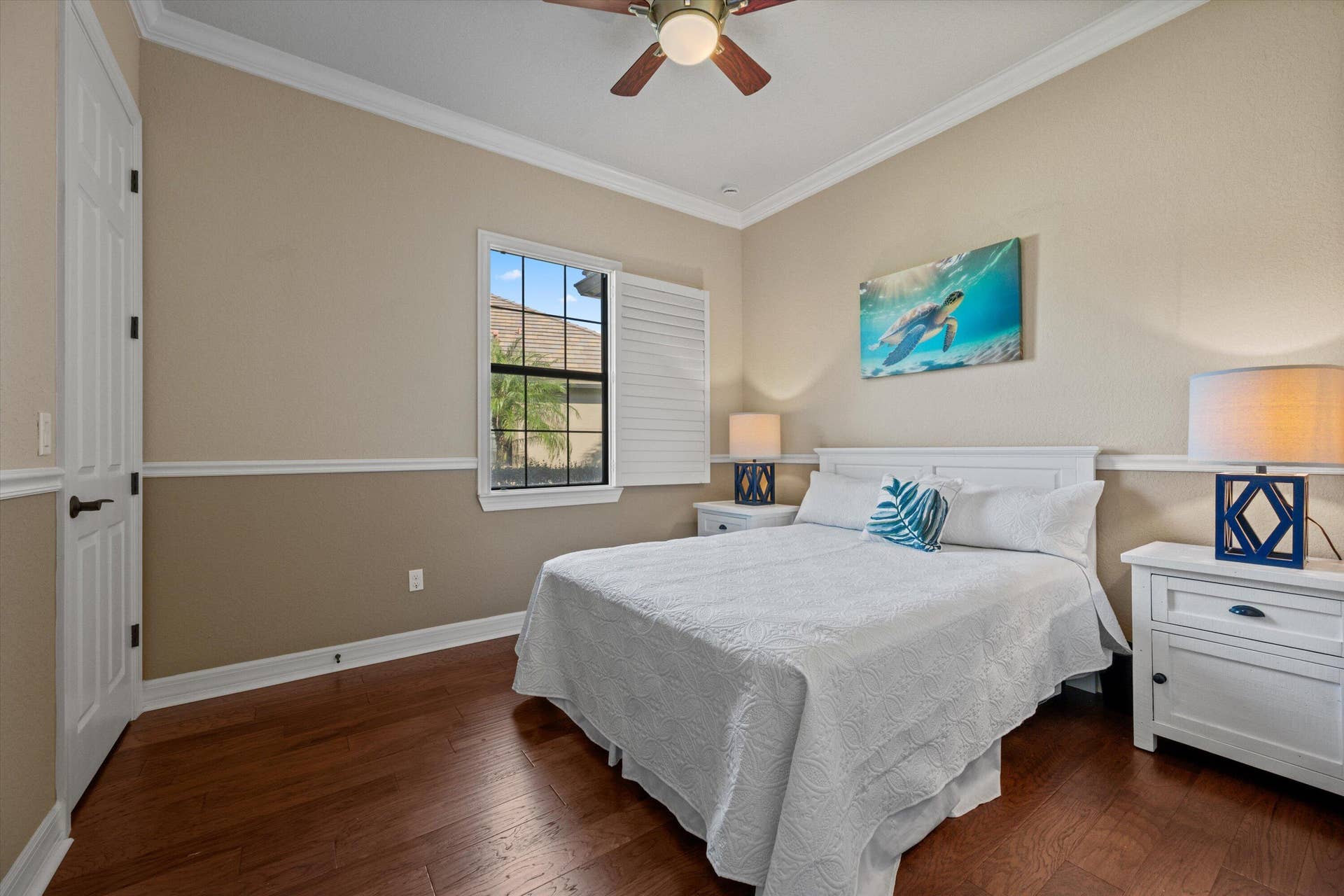 Wood-finish flooring, multi-pane window with plantation shutters, ceiling fan, and chair rail molding