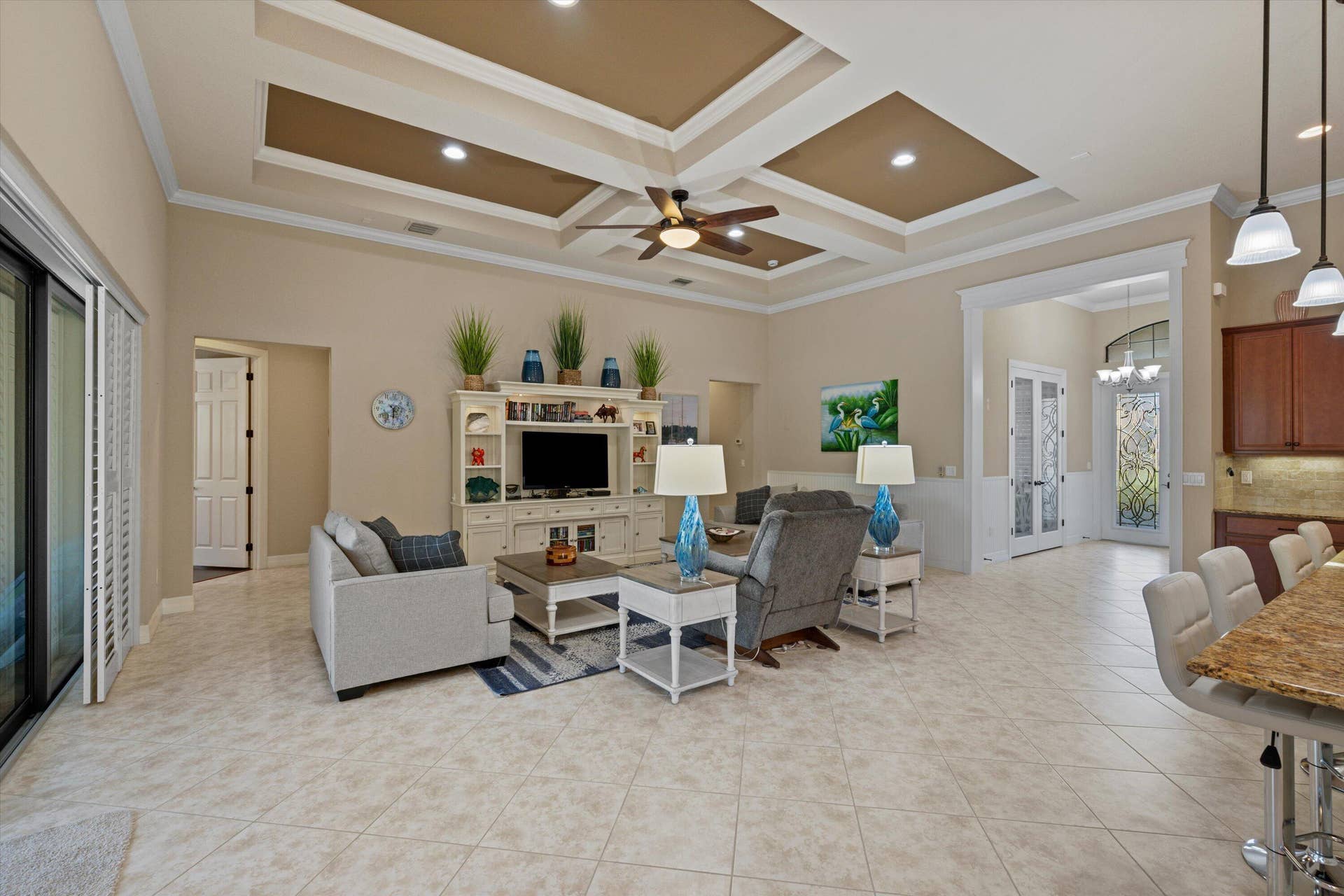 Tray ceiling with recessed lighting and a central ceiling fan, built-in media cabinetry, tile flooring, stone-surfaced kitchen island, and pendant light fixtures