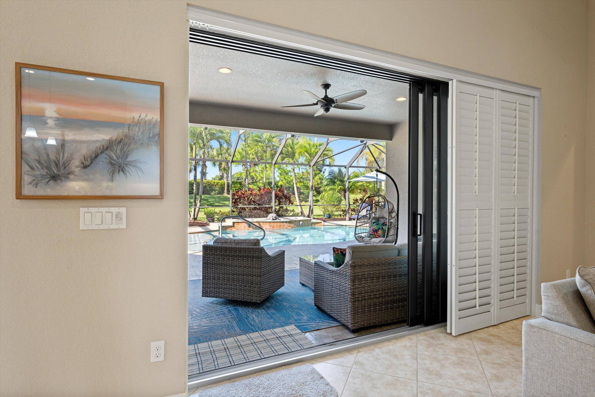 Multi-panel sliding glass doors with white plantation shutters, recessed ceiling lighting, and a covered lanai featuring a ceiling fan and screen enclosure with a pool