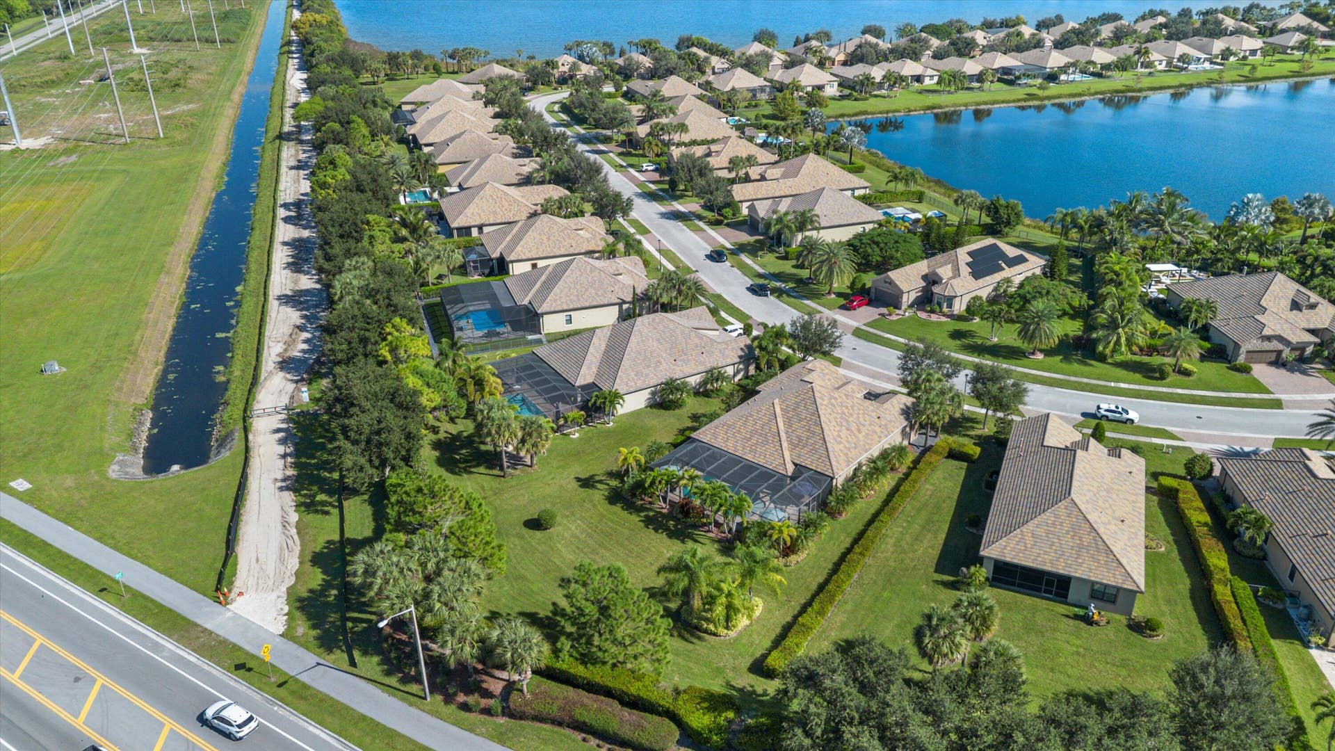Aerial perspective of residential community featuring homes with hip-style rooflines, screened-in pool enclosures, paved street infrastructure, and proximity to a large body of water
