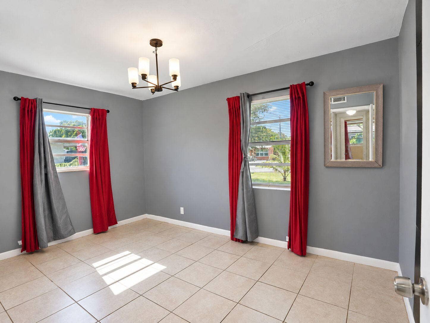 1805 NW 13TH Court, Fort Lauderdale, FL 33311 Neutral-toned interior space featuring light-colored ceramic tile flooring, dual windows with black curtain rods, and a multi-arm modern chandelier