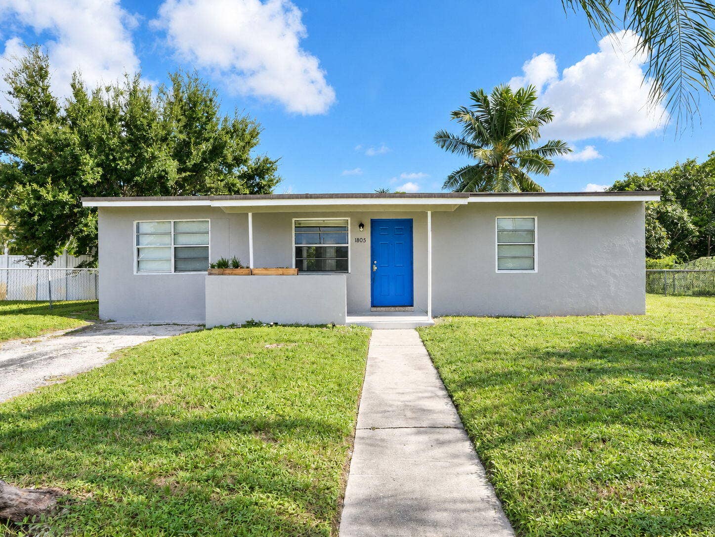 1805 NW 13TH Court, Fort Lauderdale, FL 33311 Single-story exterior featuring a neutral stucco facade, bright blue front door, covered front entryway, and concrete walkway