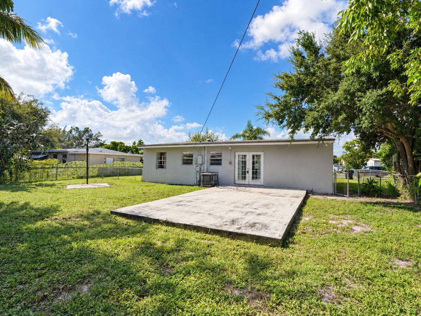 1805 NW 13TH Court, Fort Lauderdale, FL 33311 Rear exterior featuring a concrete patio, grassy yard, chain-link perimeter fencing, and double glass-panel doors