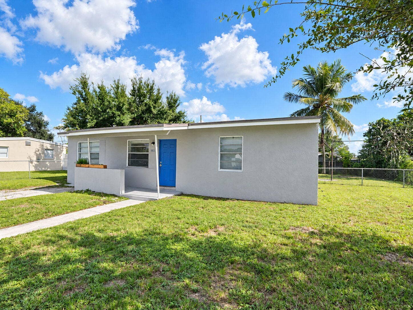 1805 NW 13TH Court, Fort Lauderdale, FL 33311 Single-story exterior featuring a neutral stucco facade, blue entry door, horizontal sliding windows, and a concrete walkway