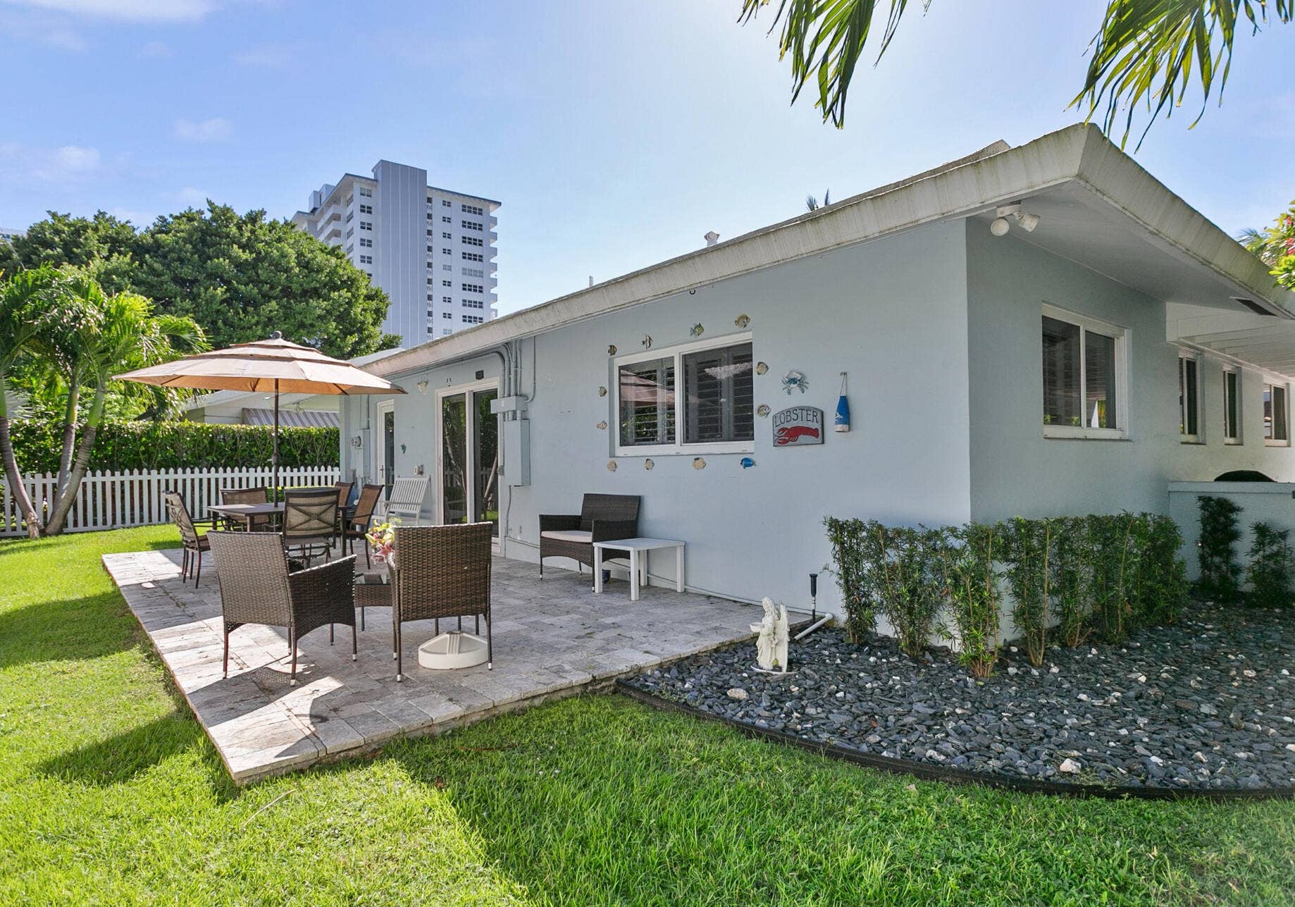 2607 SE 21ST Street, Fort Lauderdale, FL 33316 Rear exterior featuring a stone paver patio, manicured lawn, white picket fencing, and low-profile landscaping