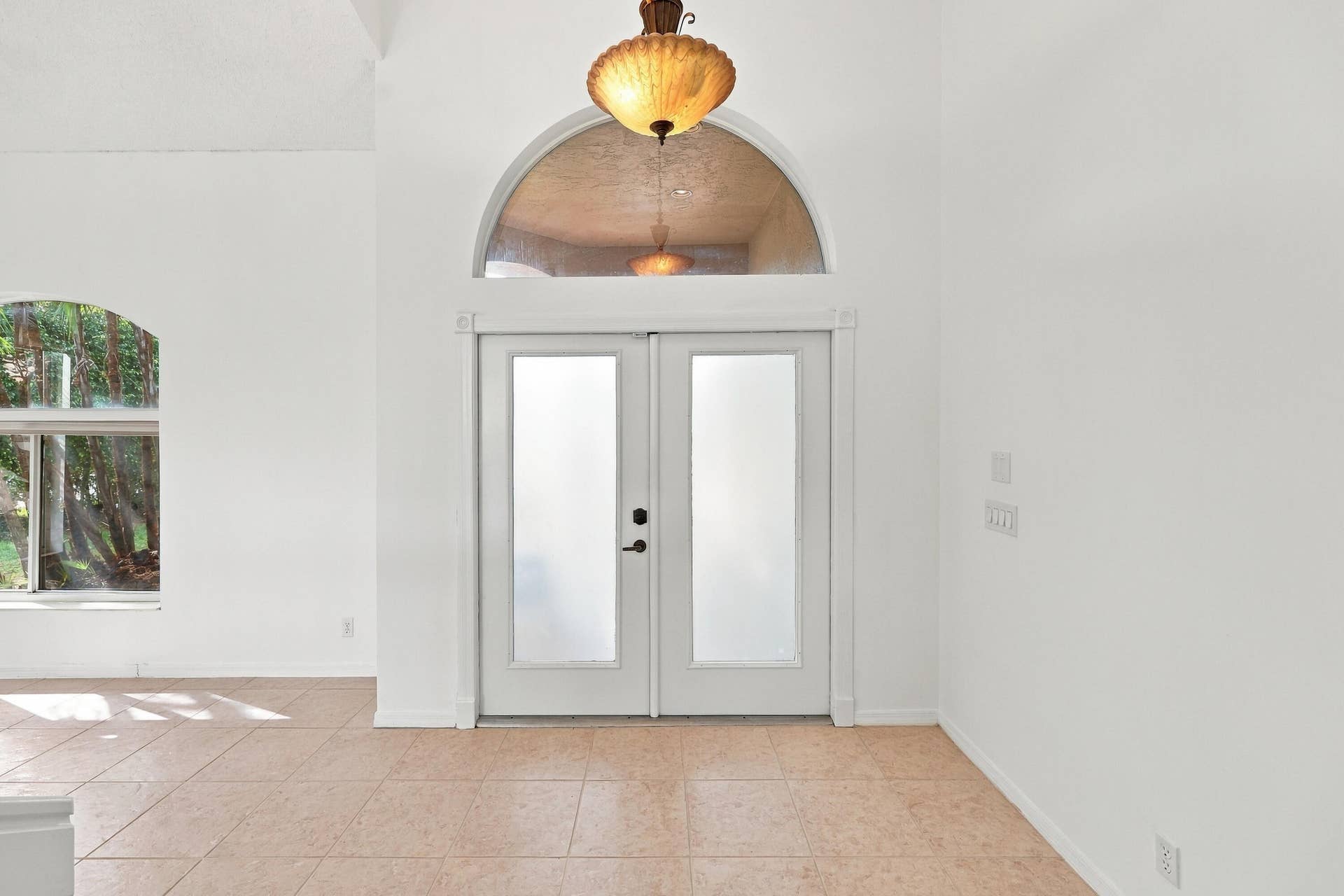 10671 St Thomas Drive, Boca Raton, FL 33498 A welcoming entrance featuring elegant double doors, a decorative arched transom window, soaring ceilings, and an abundance of natural light.
