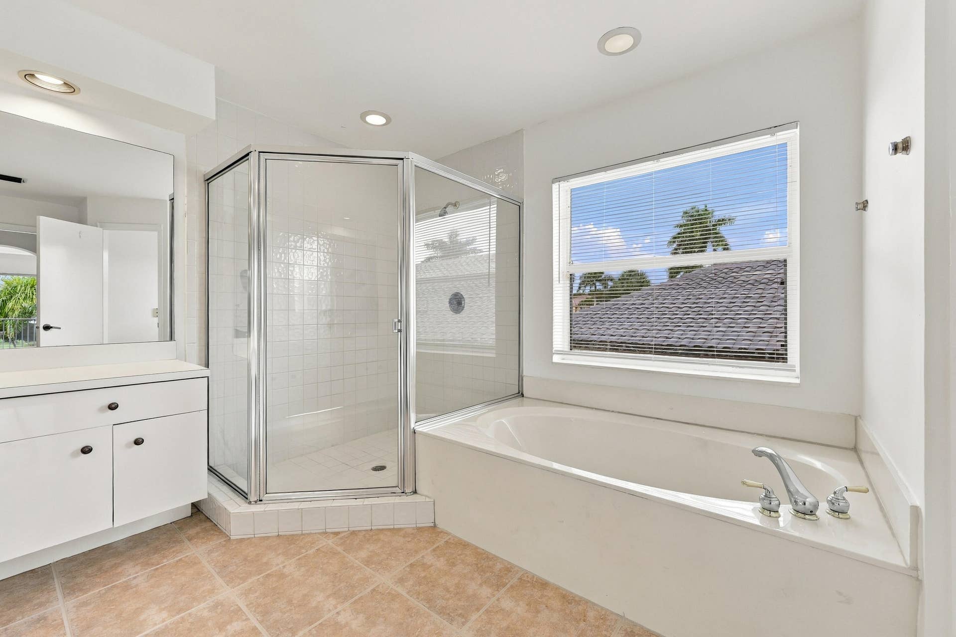 10671 St Thomas Drive, Boca Raton, FL 33498 A spacious primary bathroom featuring a relaxing soaking tub beneath a large window, a glass-enclosed shower, and neutral finishes that create an inviting atmosphere.