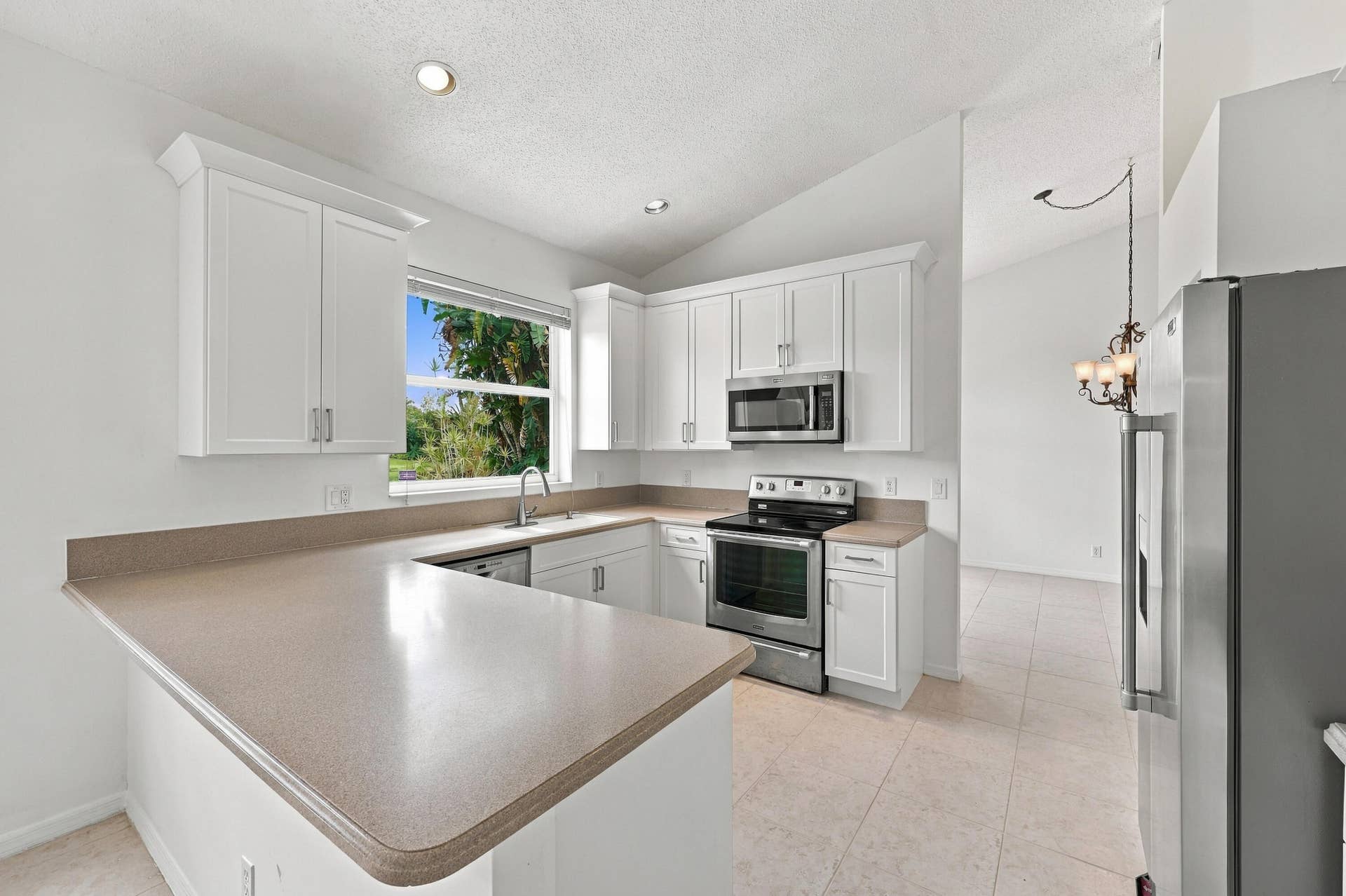 10671 St Thomas Drive, Boca Raton, FL 33498 A thoughtfully arranged kitchen offering extensive counter space, white cabinetry, stainless steel appliances, and convenient access to the adjoining breakfast area.